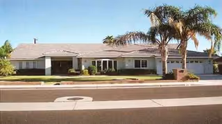 Single-story facility with beige exterior, manicured lawn, and palm trees at the front.