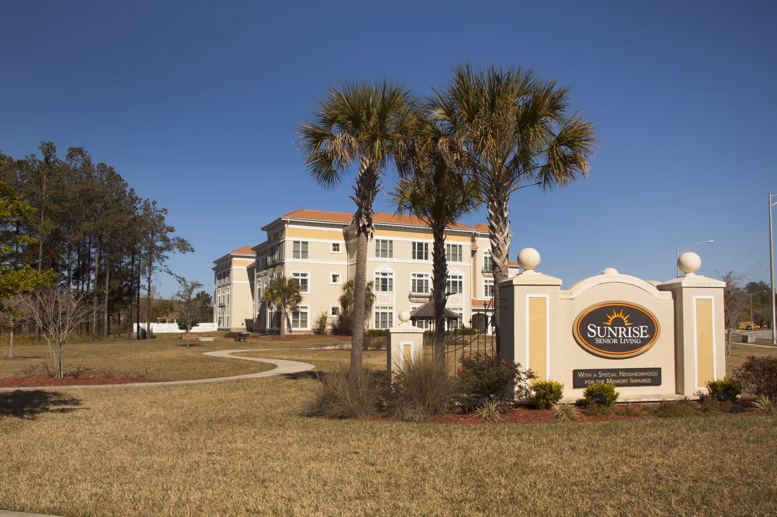 Front view of Sunrise Senior Living facility with palm trees and signage.