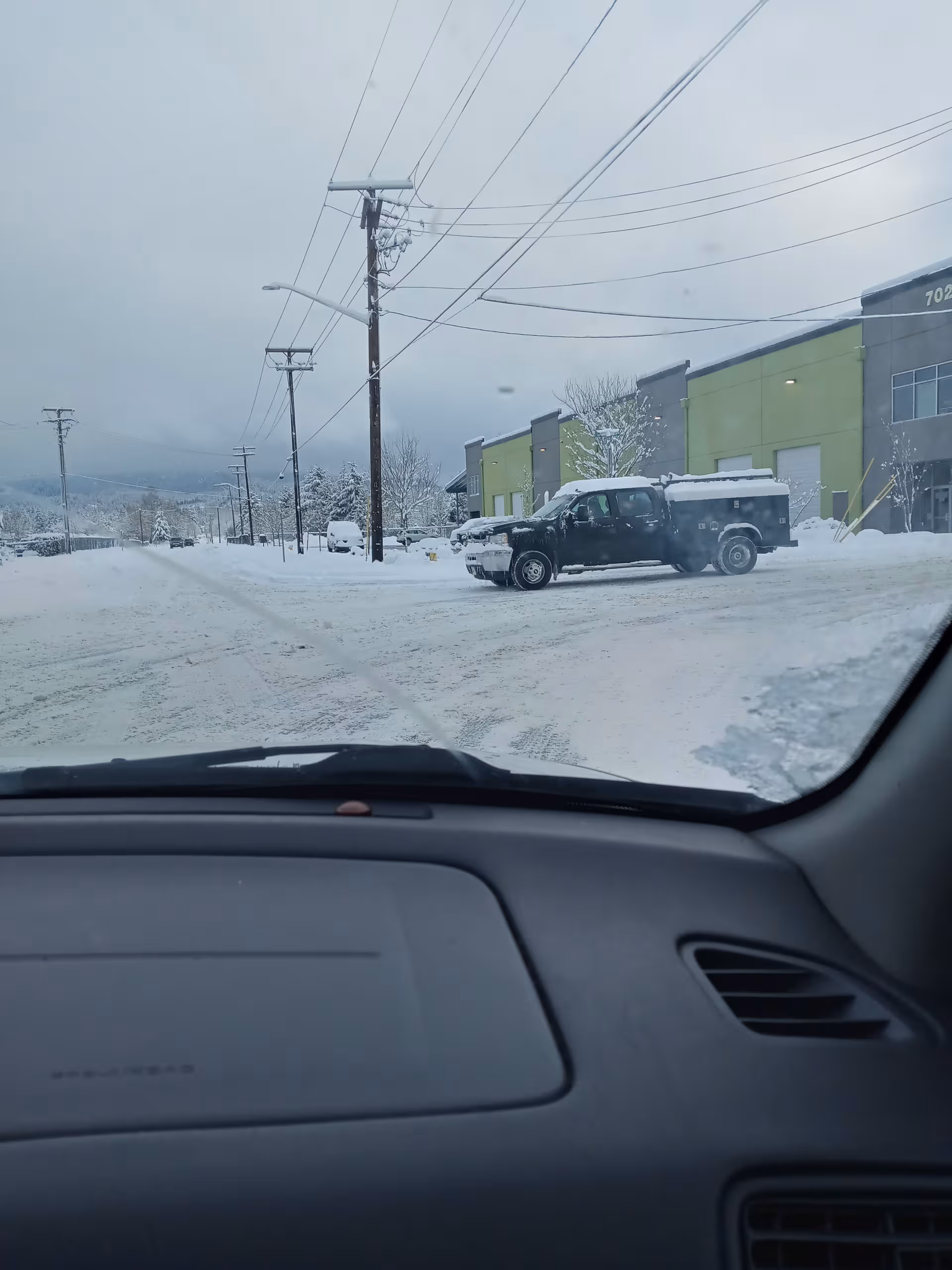 Snow-covered street view of a green-gray facility exterior with a parked truck.