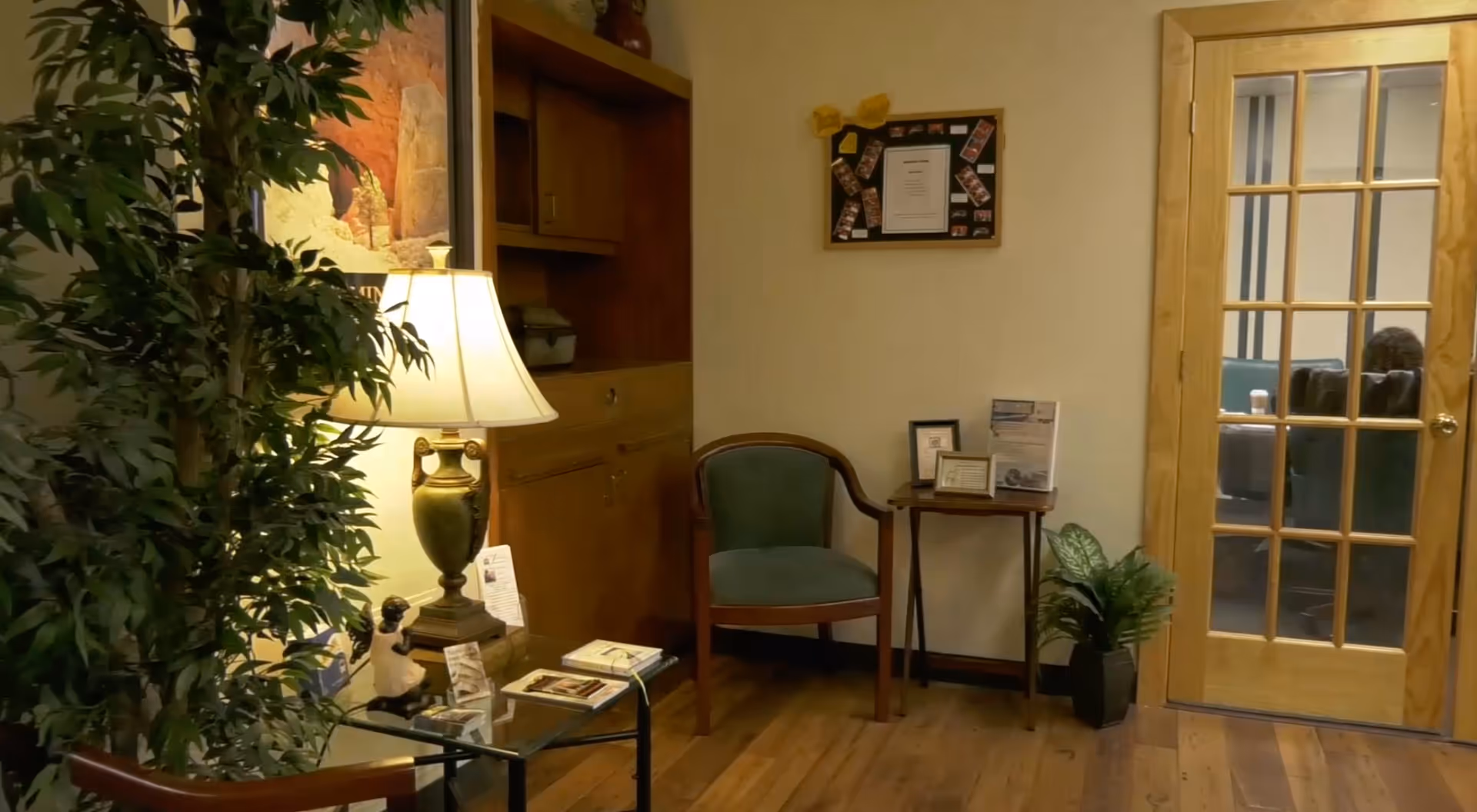 Cozy interior lobby with a lamp, green chair, plant, and glass-pane door.