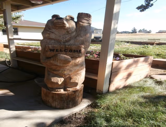 Carved wooden hand-shaped welcome statue on a covered outdoor porch beside planters.