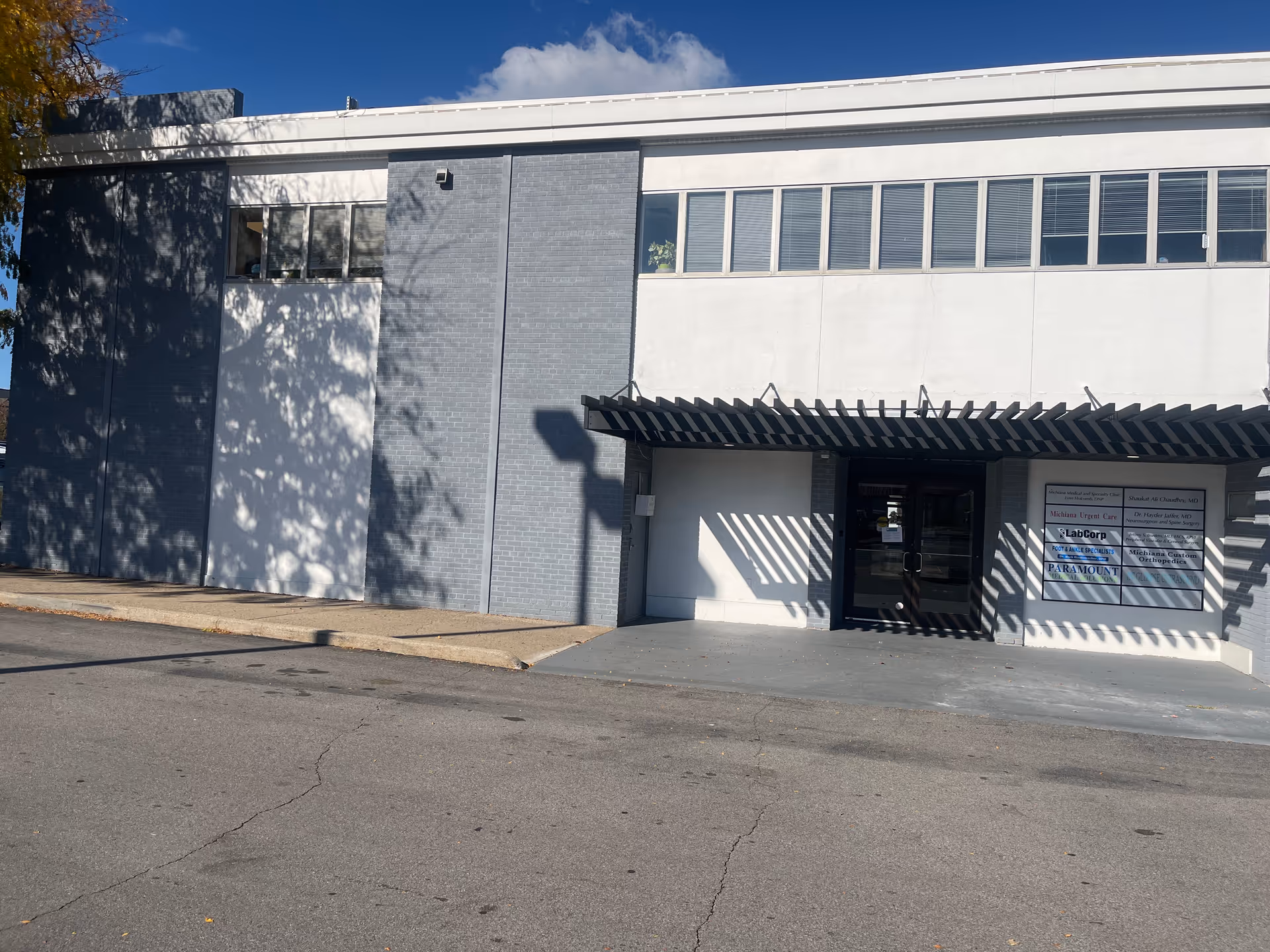 Modern gray exterior building with a front entrance, glass doors, and striped shadow awning.