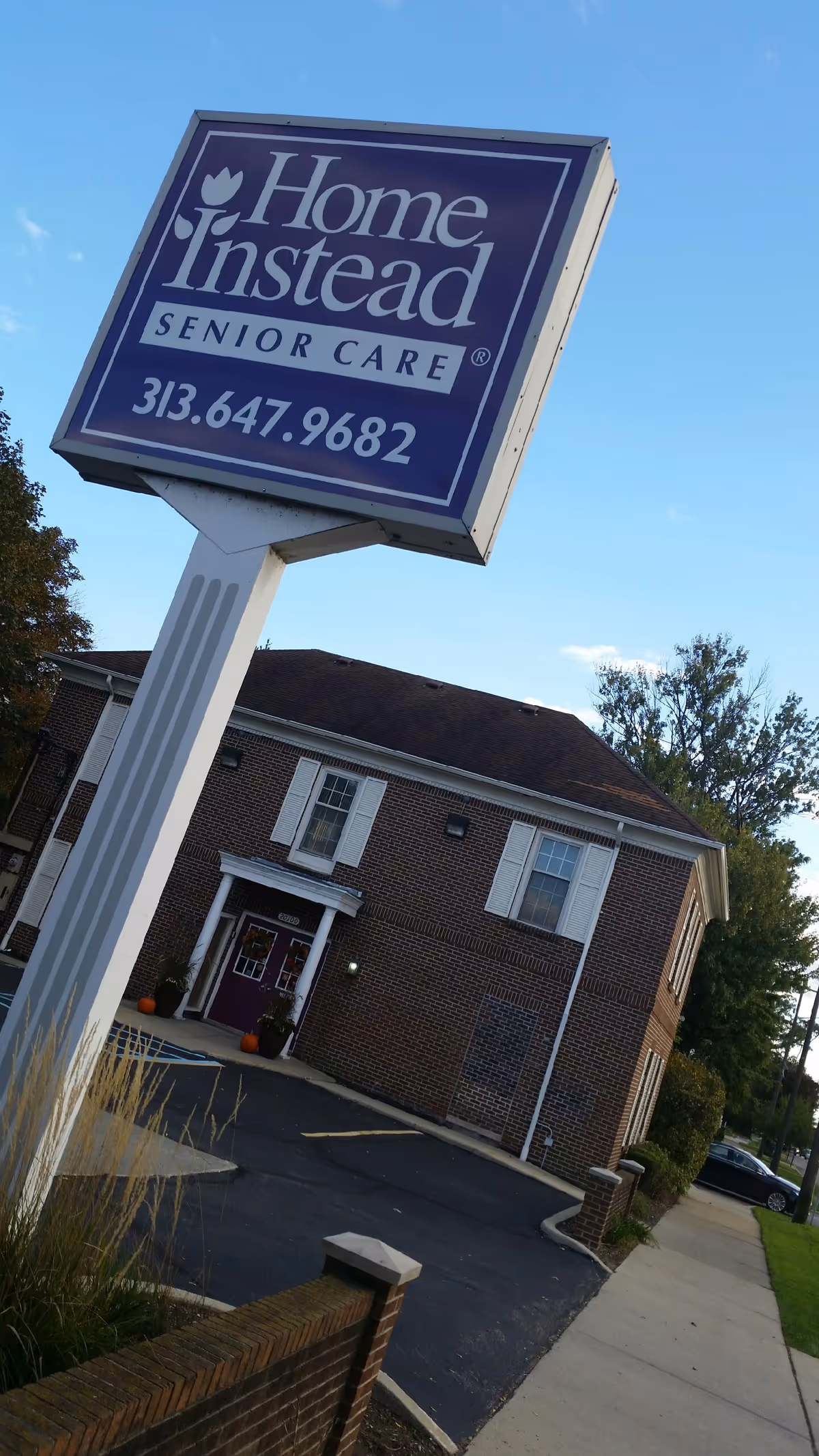 A tilted Home Instead Senior Care sign stands beside a brick facility entrance.