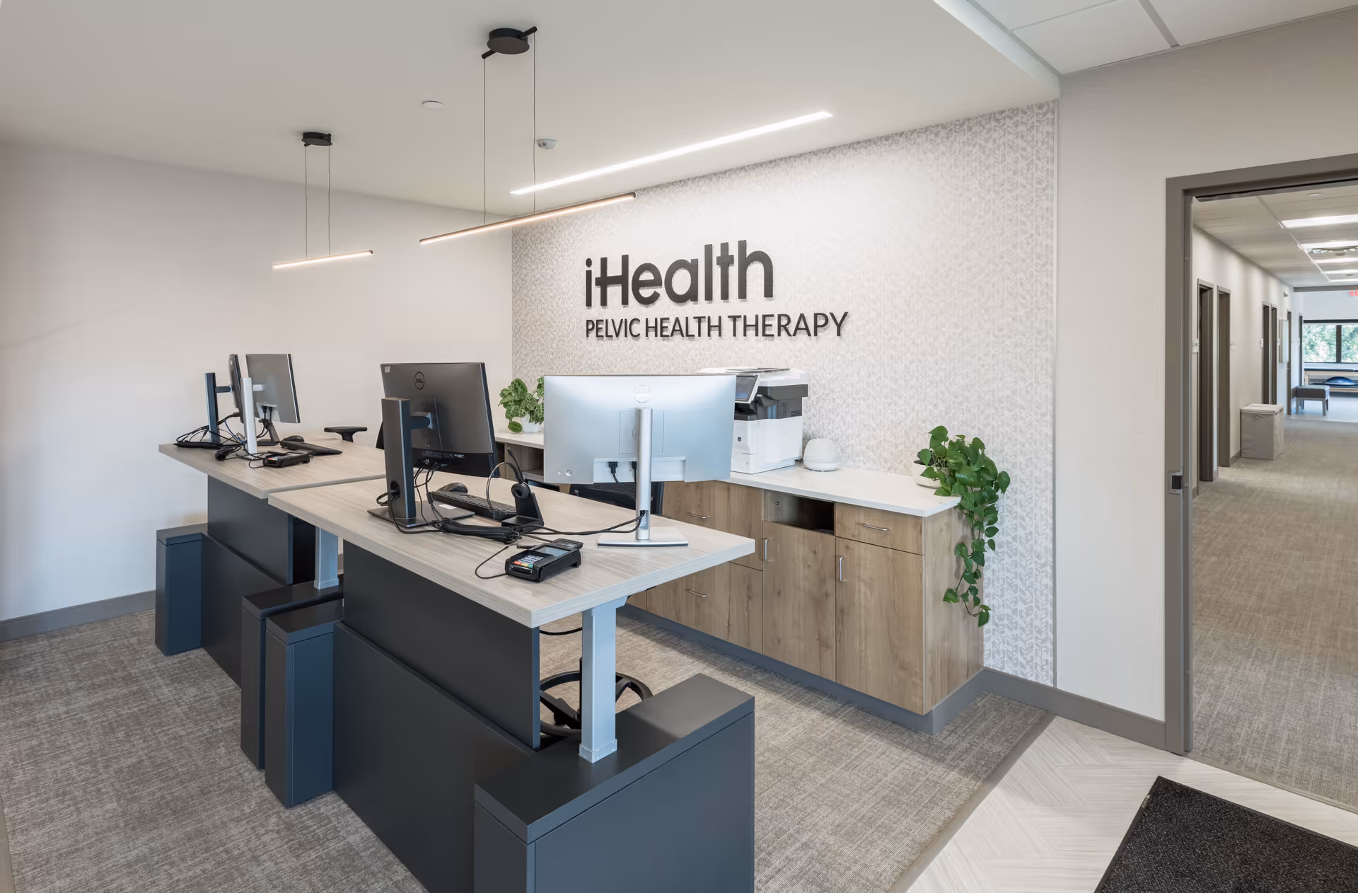 Modern reception desk with dual computer stations and iHealth Pelvic Health Therapy sign.