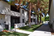 Two-story senior living building exterior with a shaded walkway and tall trees.