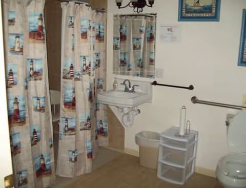 Accessible bathroom with shower curtain, sink, toilet, and grab bars in a senior facility.