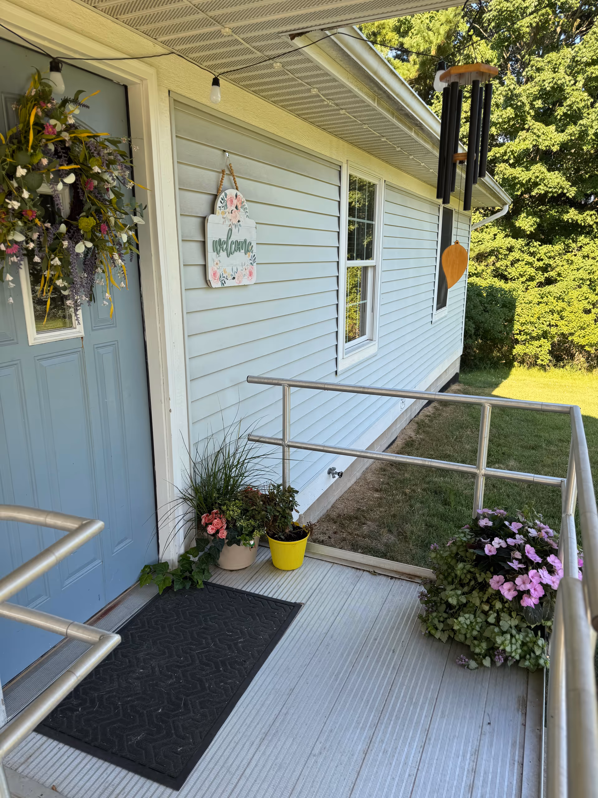Front entrance of a light blue building with a ramp, flowers, and a welcome sign.