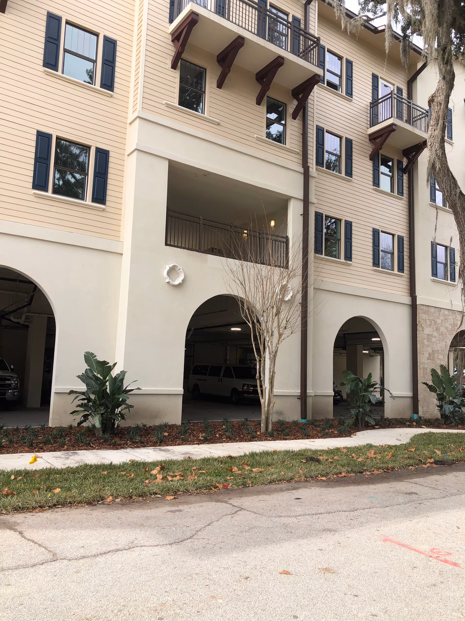 Exterior view of a beige multi-story senior living building with arches and balconies.