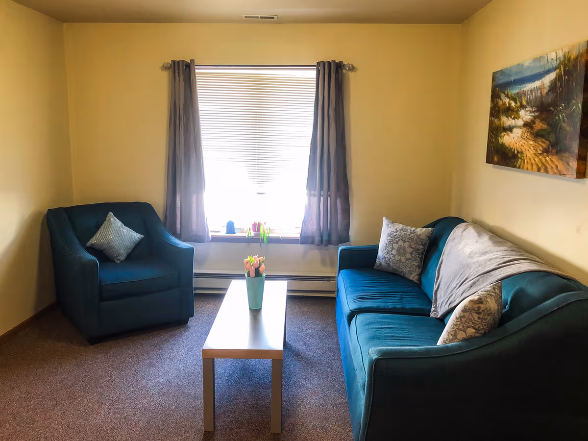 Cozy living room with teal seating, window, and a small coffee table with tulips.