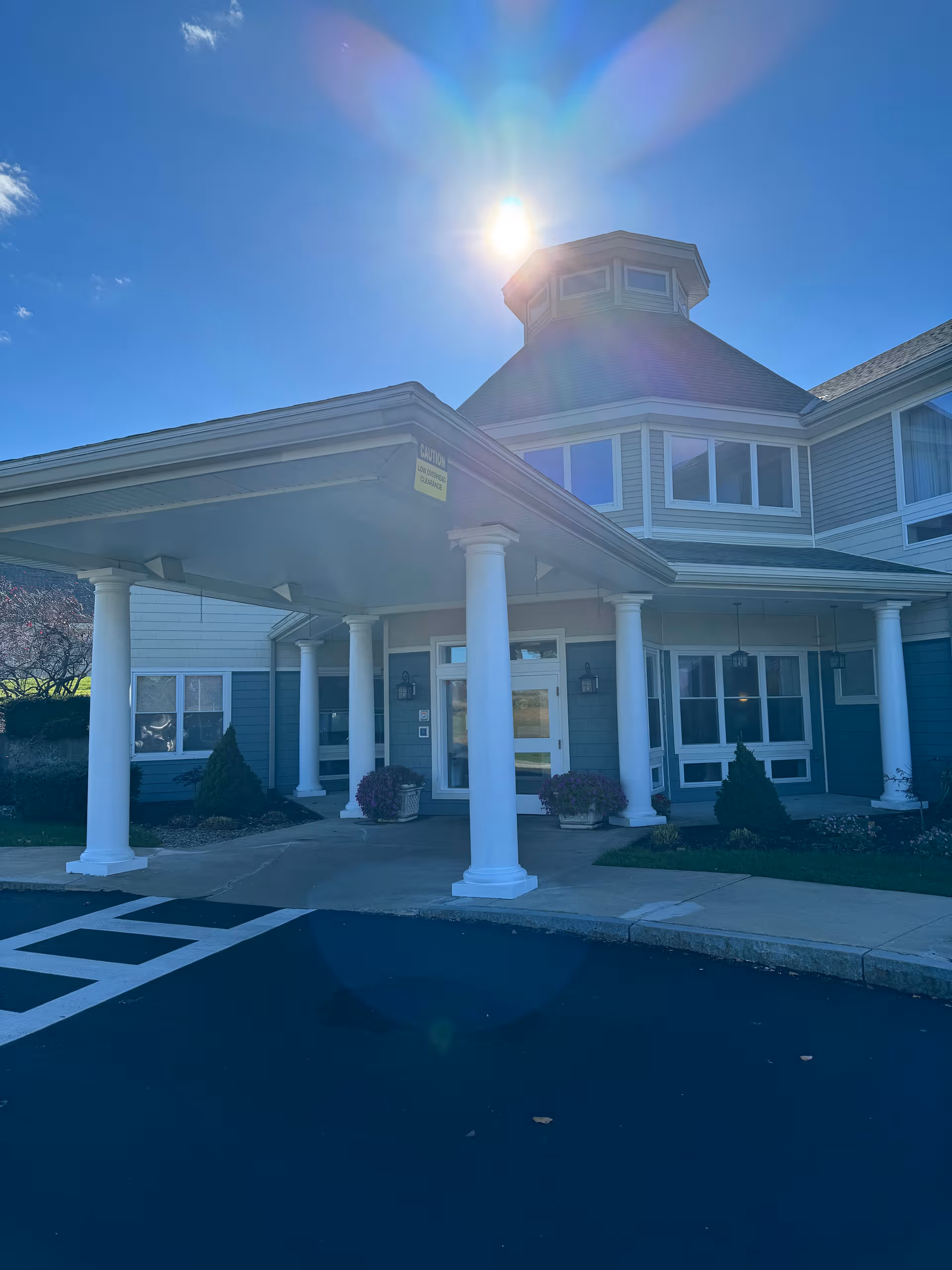 Exterior of Sterling Village senior living with a covered entrance and white columns against blue sky.