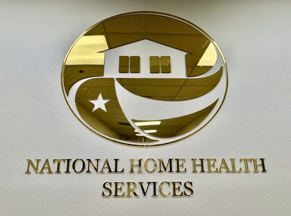 Gold circular logo with house symbol and National Home Health Services text on a white wall.