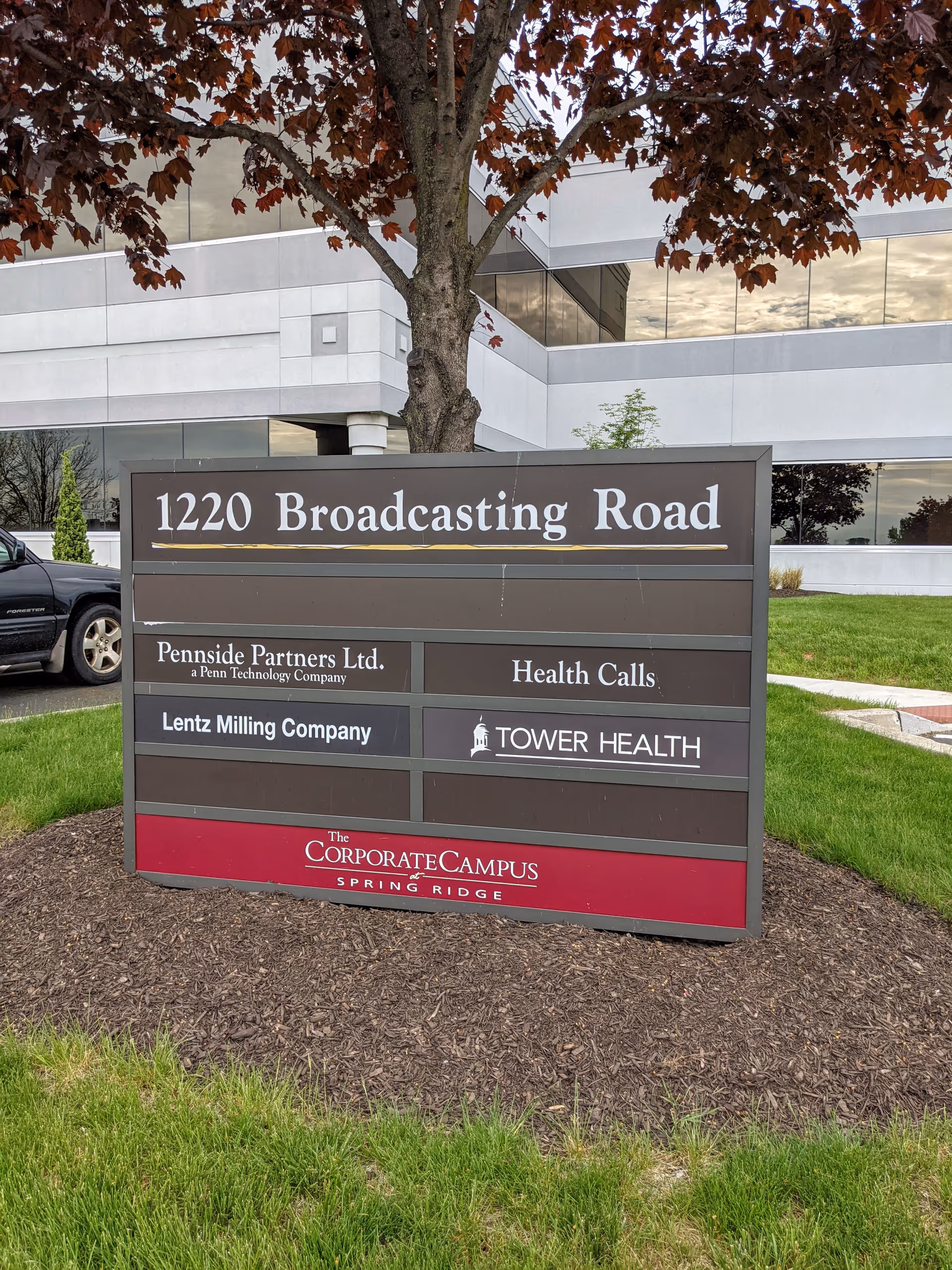 A large outdoor sign with Health Calls and other names in front of a modern building.