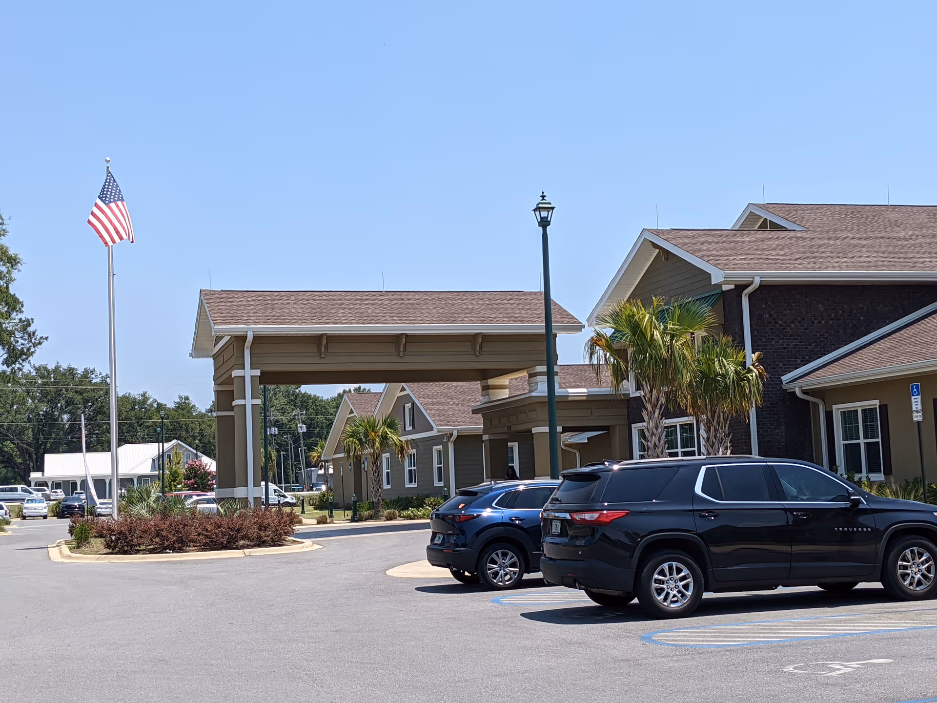 Exterior view of De Luna Health and Rehabilitation Center with a flag, porte-cochère, and parked cars.