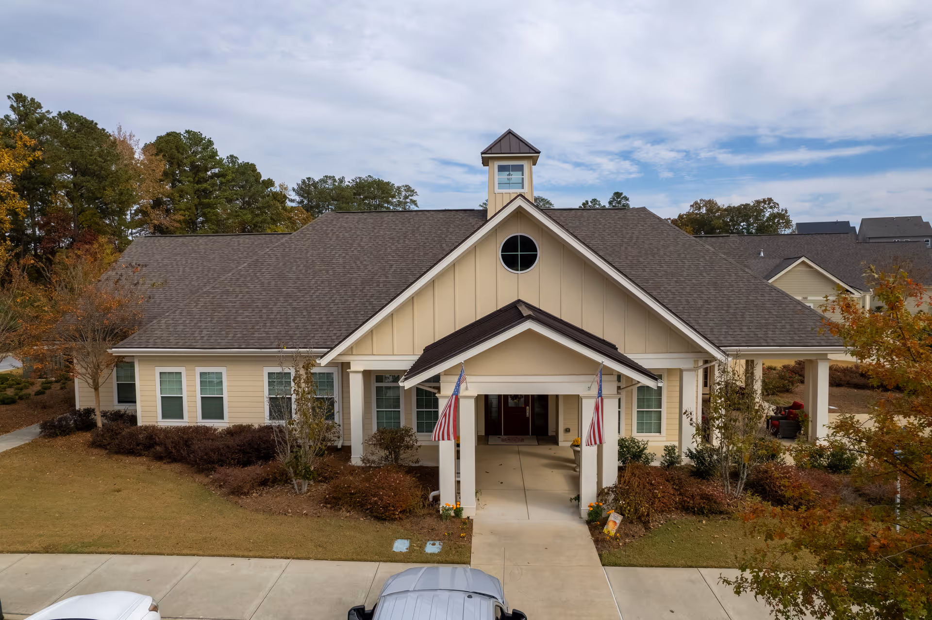 Exterior view of a single-story senior living facility with a covered entrance and flags.