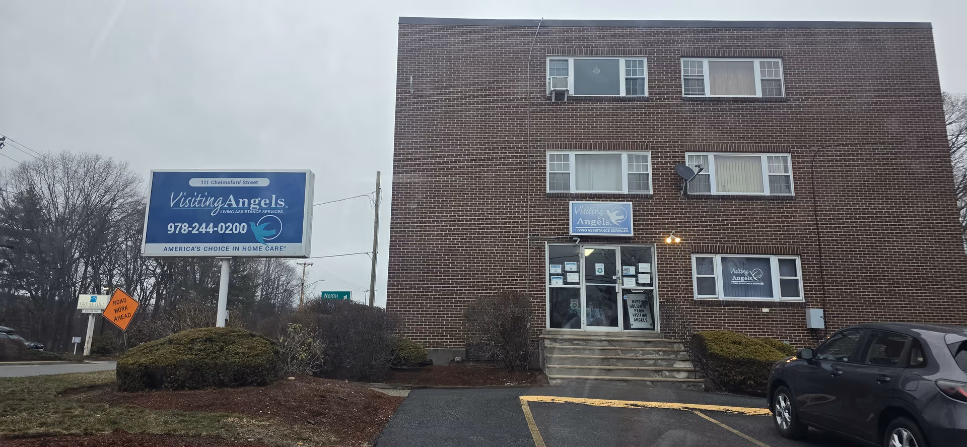 A brick, three-story building with Visiting Angels signage, a parking lot, and a front entrance.