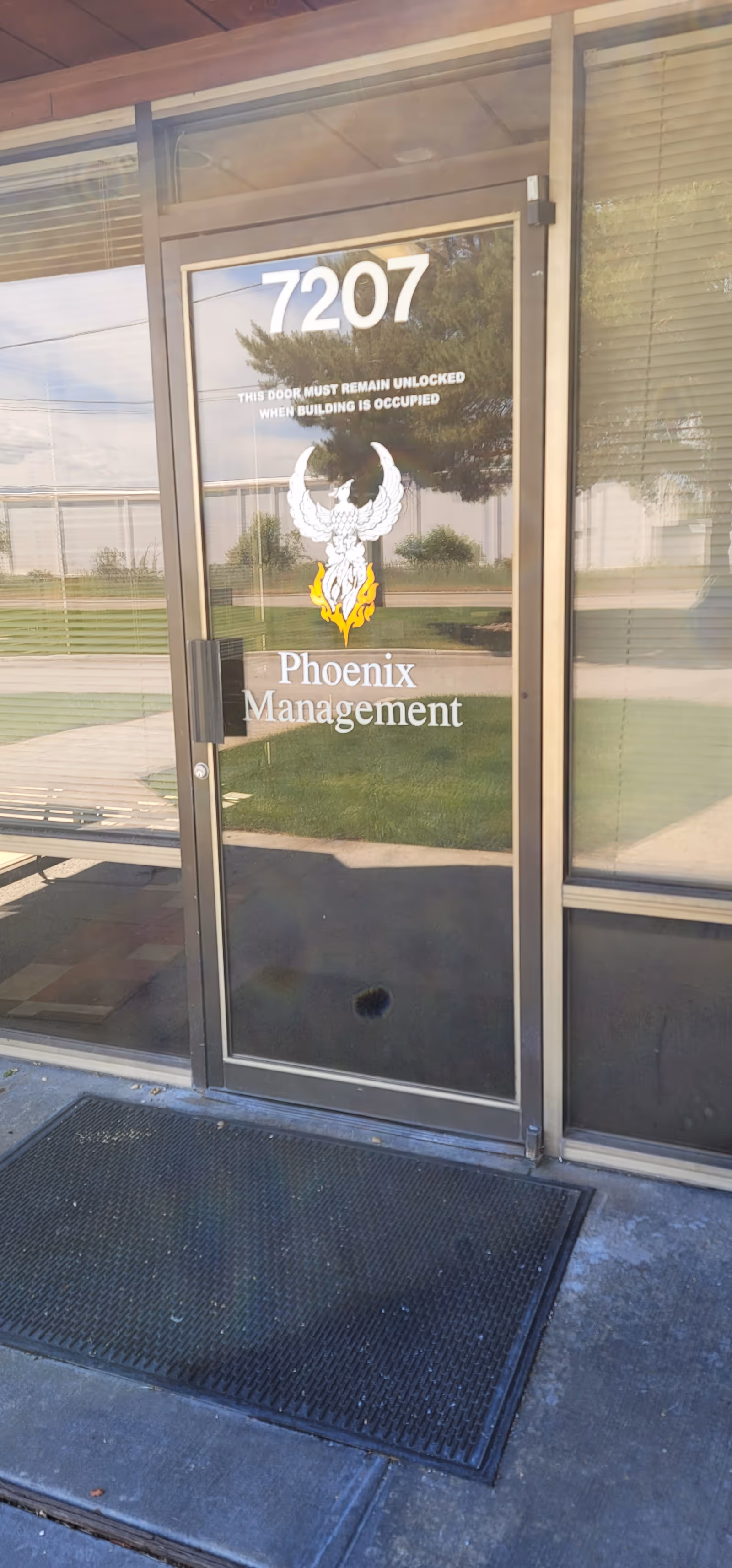 Glass entrance door labeled 7207 with Phoenix Management logo visible outside building.
