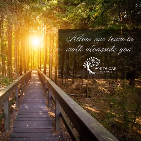 Sunlit wooden boardwalk through a forest with a White Oak Hospice sign.