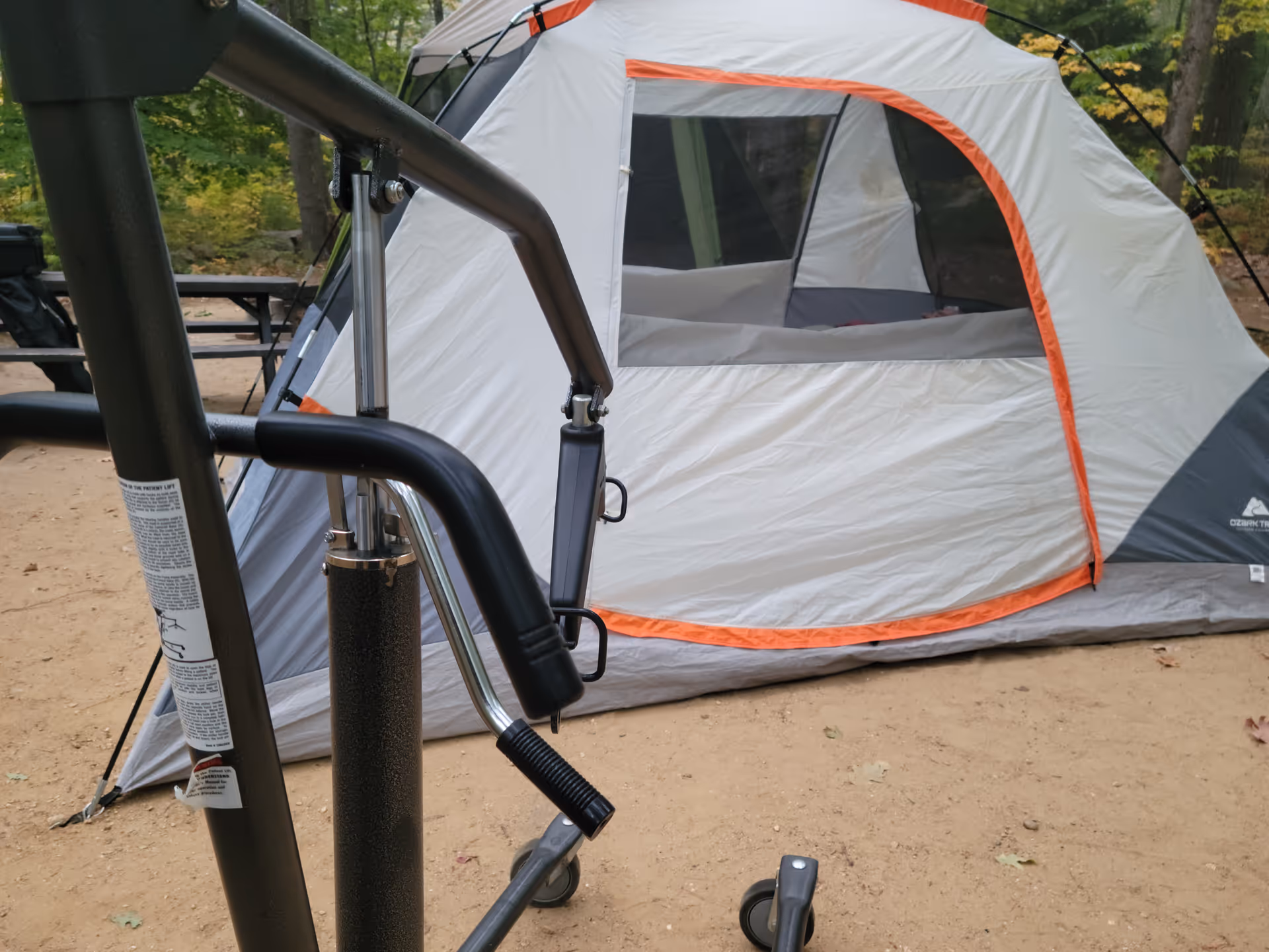 Outdoor camping scene with a white tent and camping gear on dirt ground.