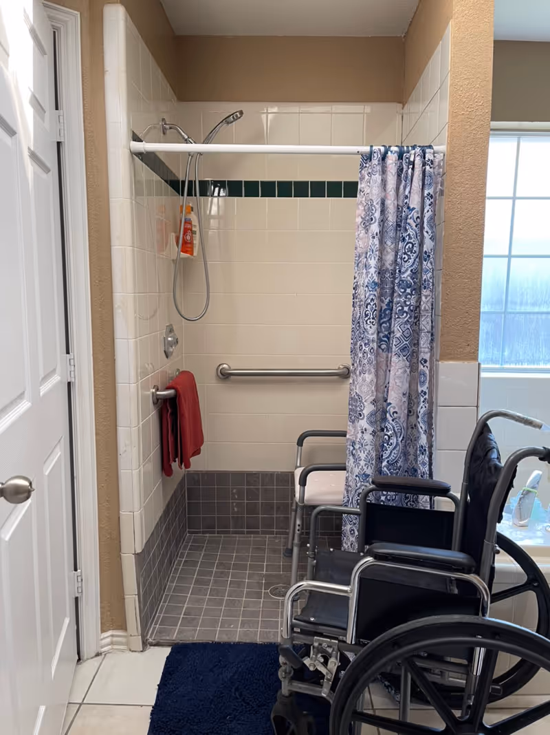 Accessible bathroom with a shower, grab bars, towel, and several wheelchairs parked inside.