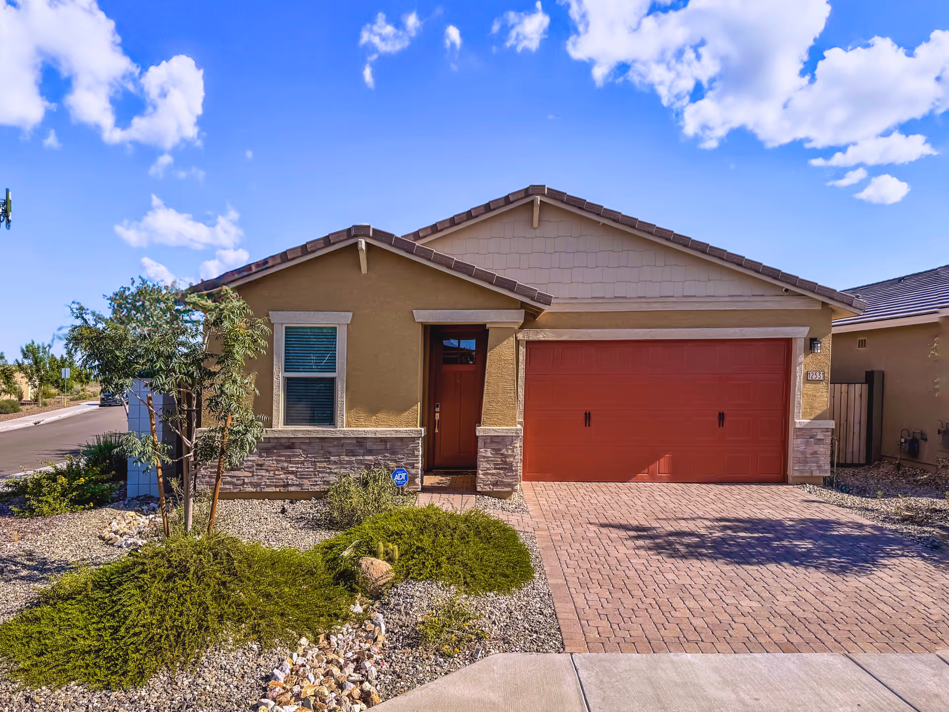 Front view of a single-story beige house with a red garage door and desert landscaping.