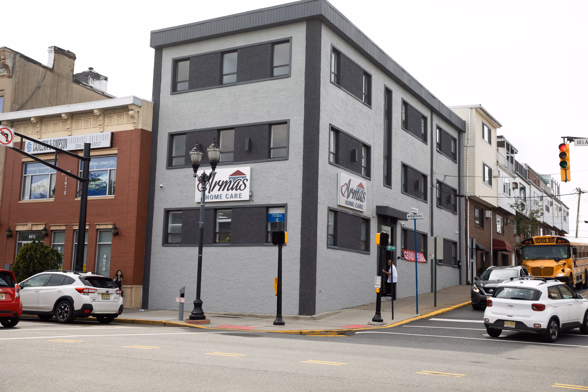 Corner street view of a gray Armas Home Care building with signage and parked cars.