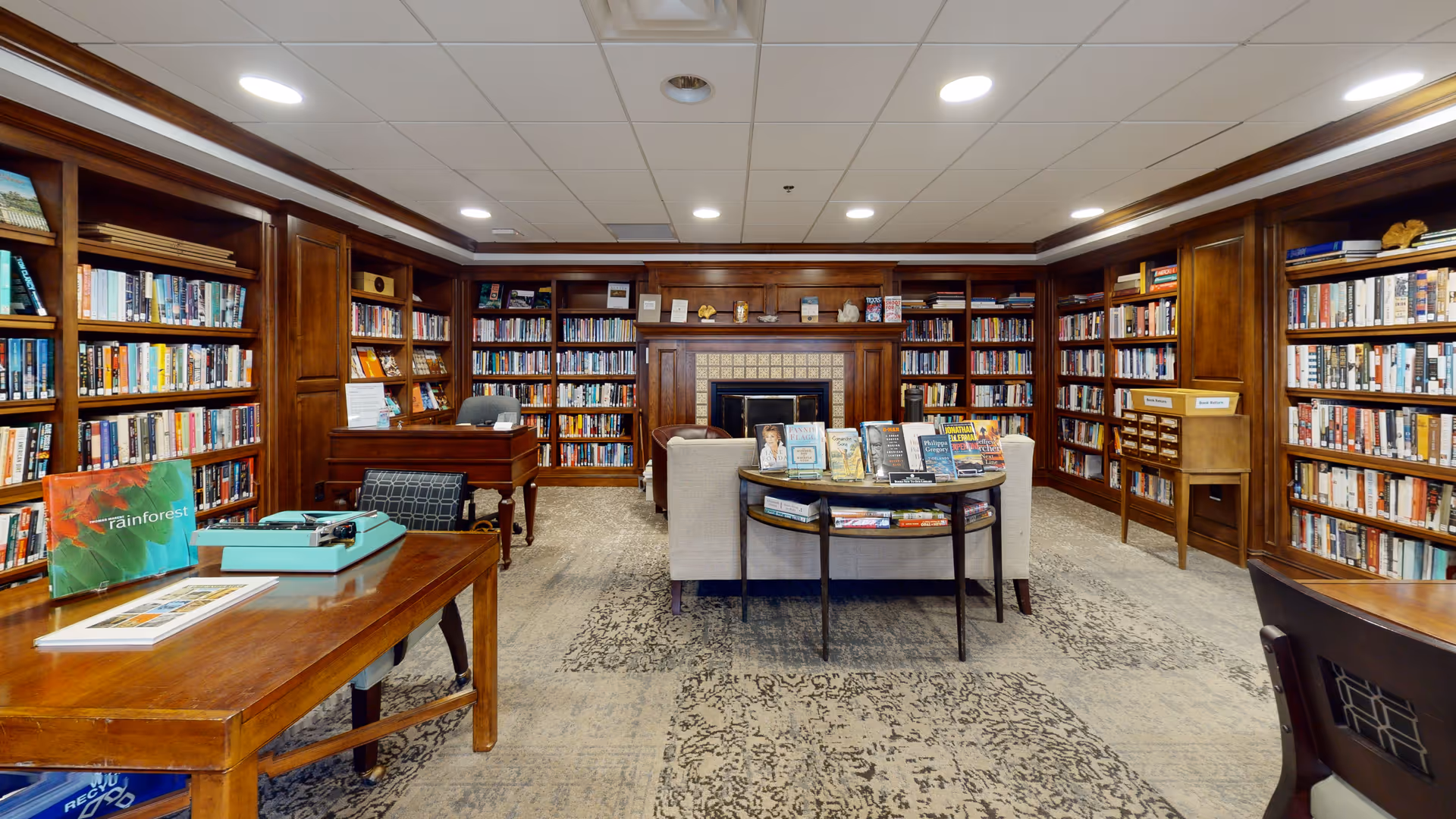 Wood-paneled library with numerous bookshelves, a central fireplace, and comfortable seating.