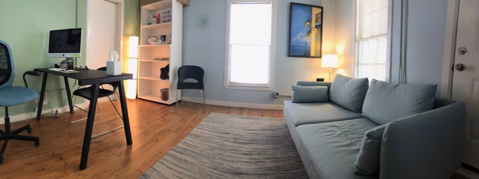 Cozy living room with a light-blue sofa, desk with computer, bookshelf, and soft lighting.