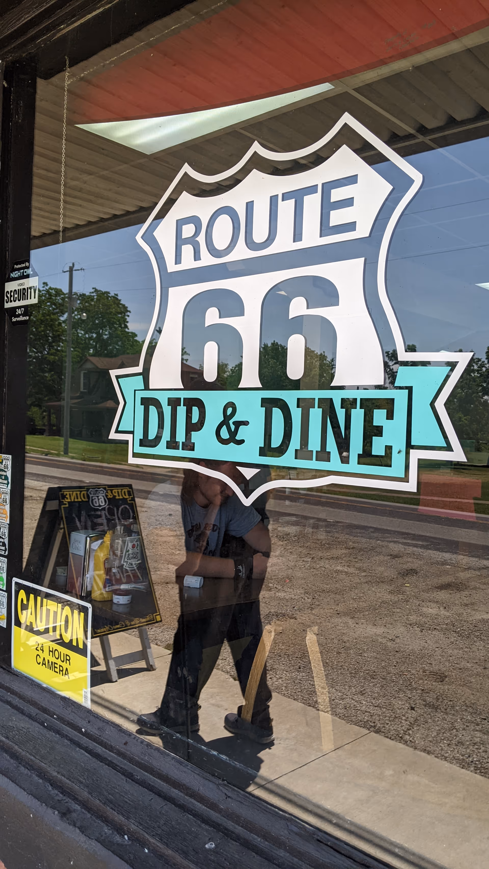Storefront window displays Route 66 Dip & Dine sign with a reflected person.