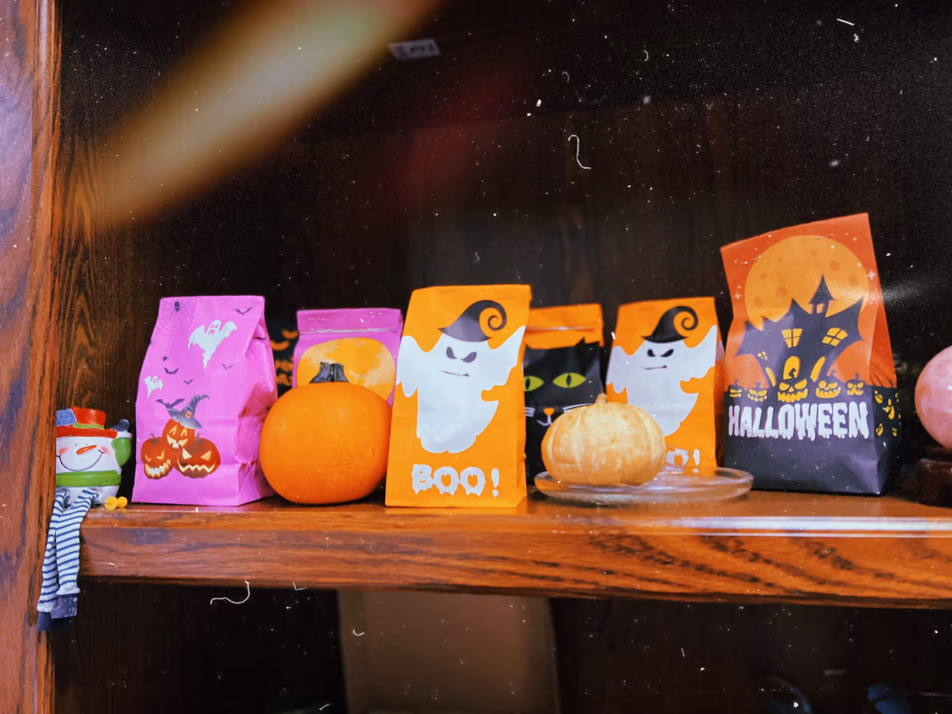 Halloween-themed gift bags and pumpkins arranged on a wooden shelf indoors.