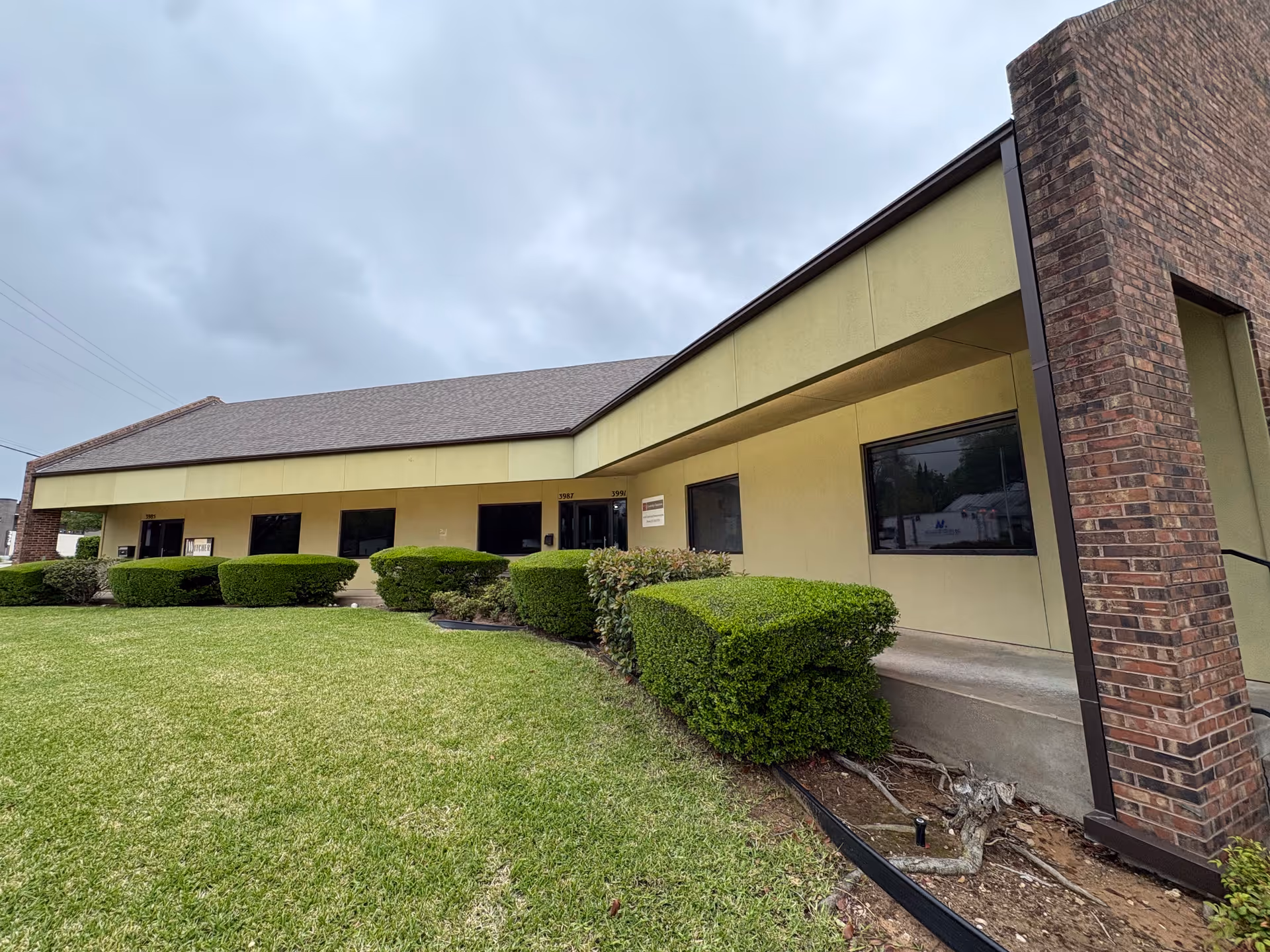 One-story beige senior living facility with trimmed hedges and a brick column.