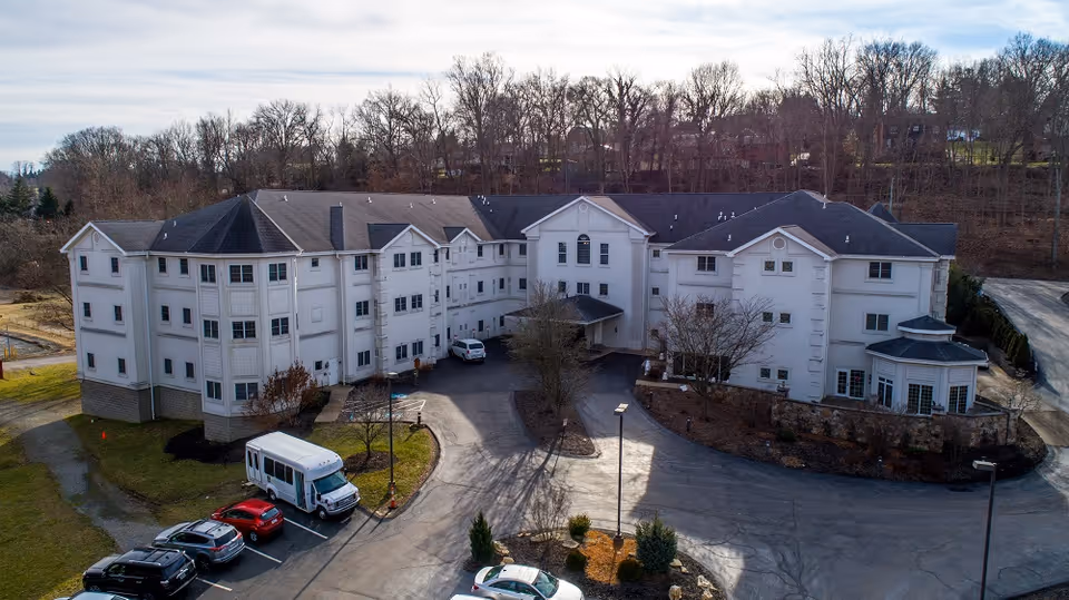 A large white senior living building with a circular driveway and parked cars.