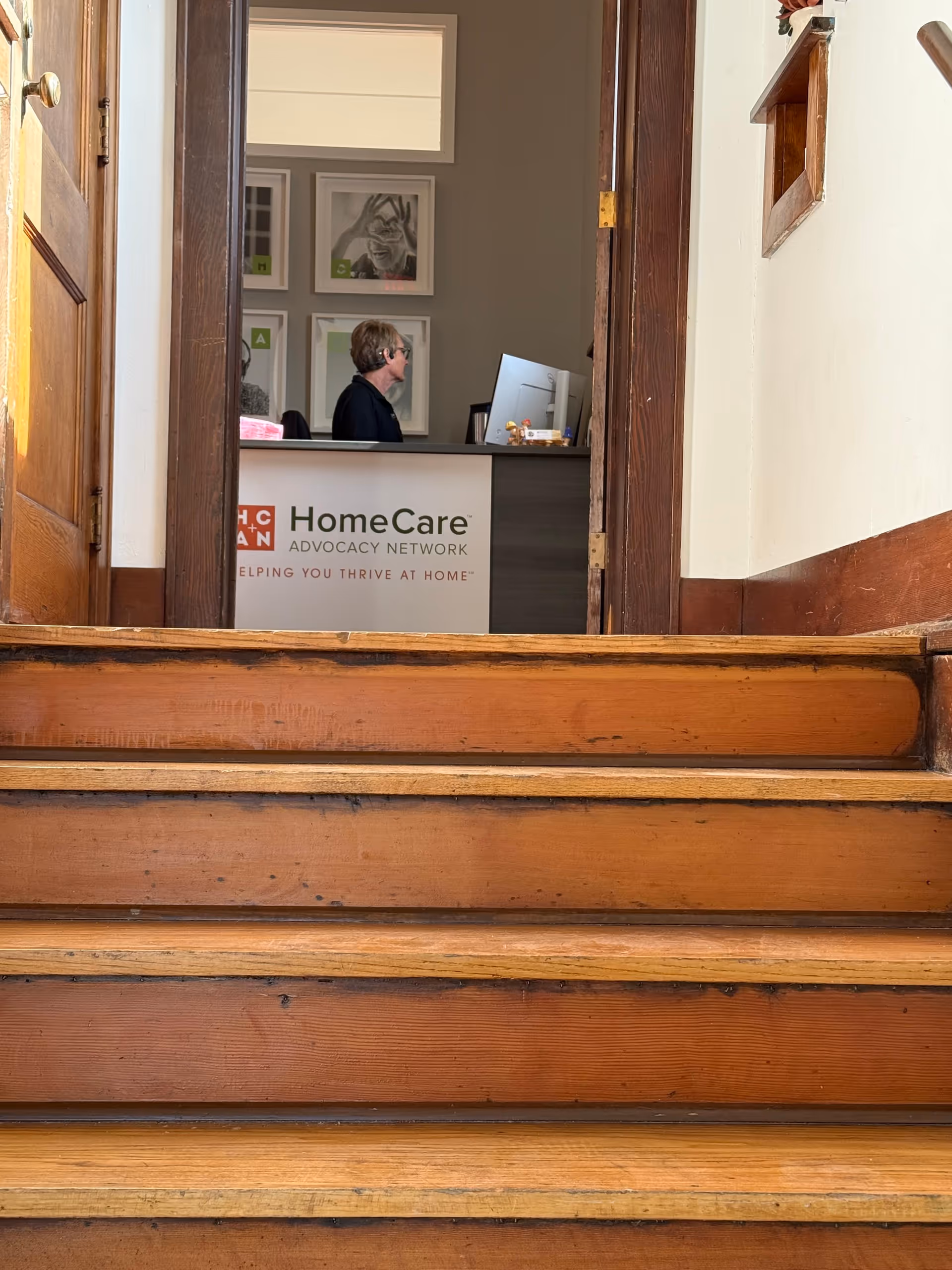 Two people sit at a desk in a reception area with HomeCare Advocacy Network signage.