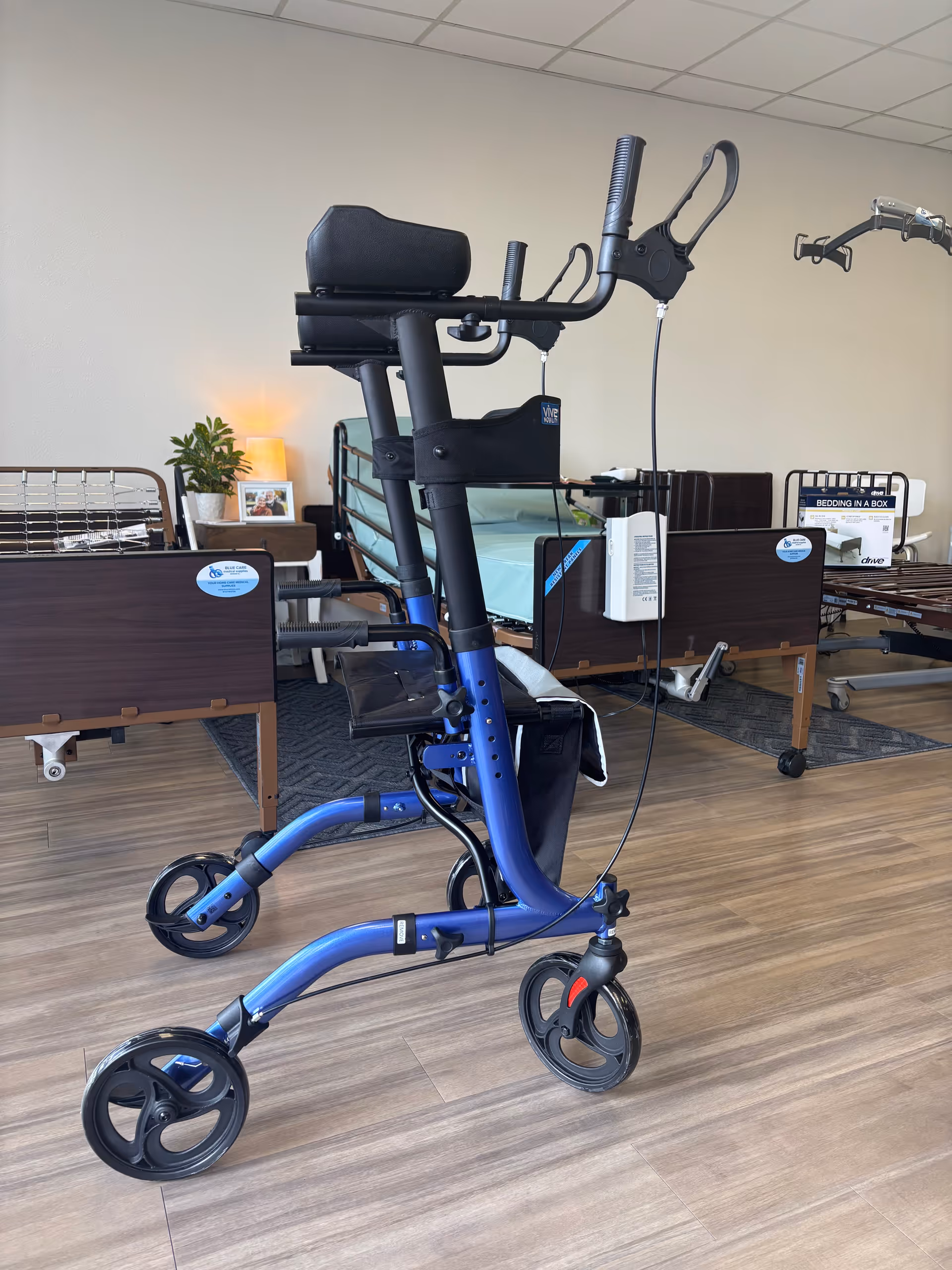 Blue mobility walker with padded seat in a room with hospital beds.