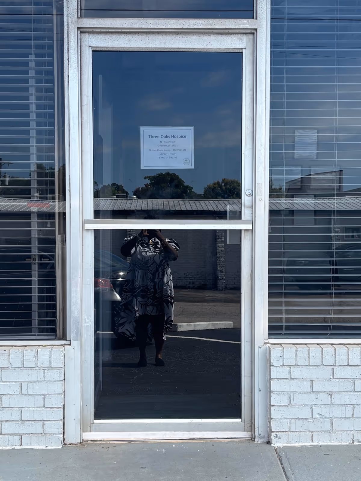 Front glass door of Three Oaks Hospice with a person reflected taking a photo.