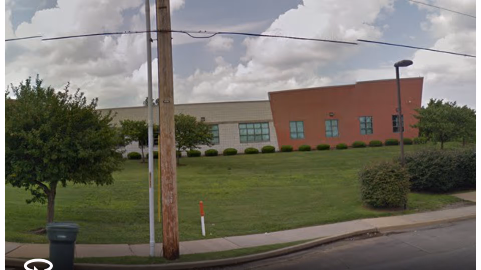 Exterior view of a facility with a green lawn, trees, and a sidewalk.