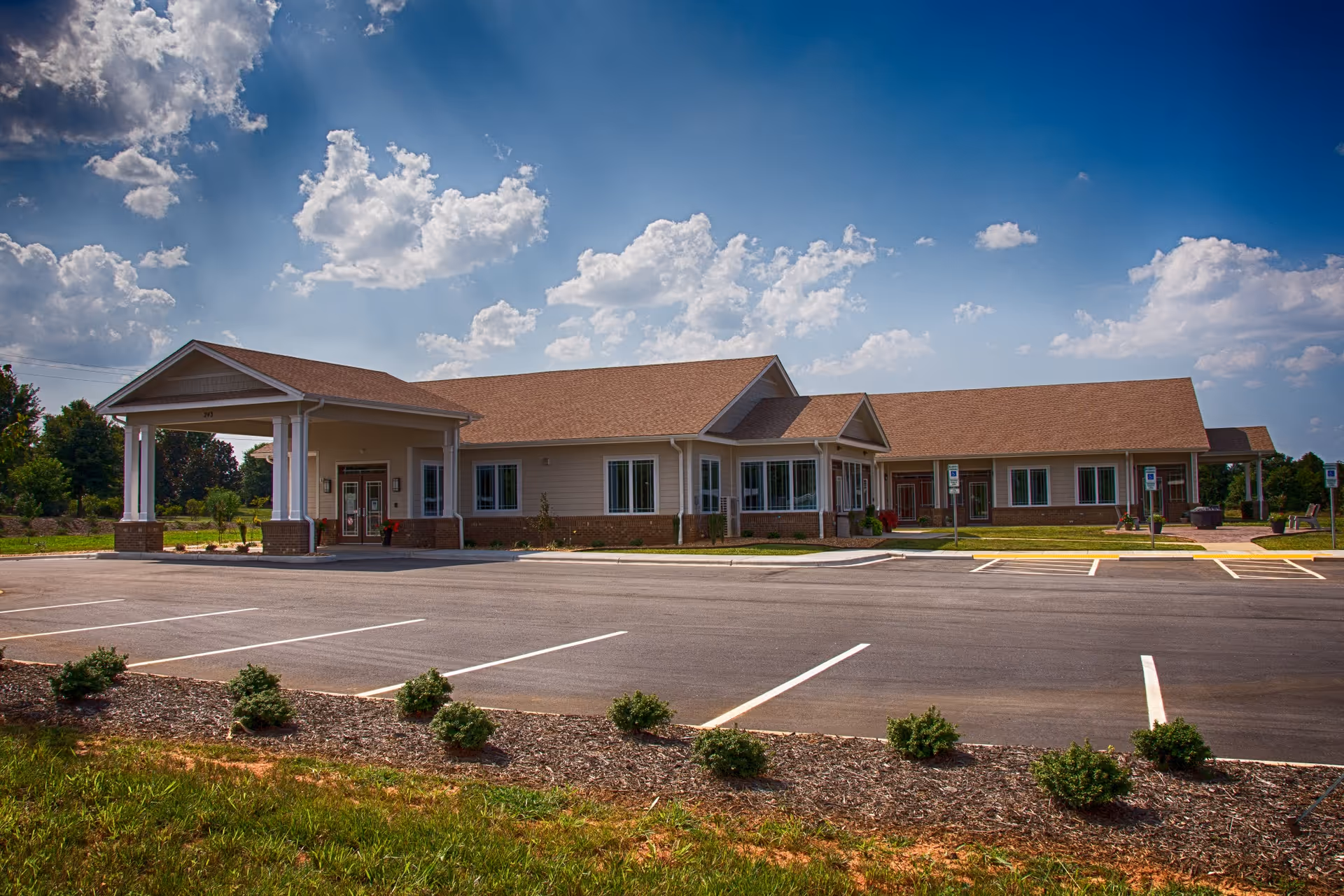 Single-story hospice care center with a covered entrance and empty parking lot under a blue sky.