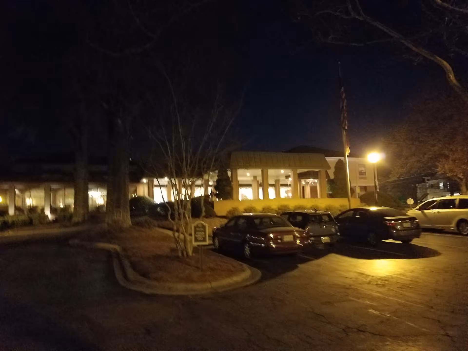 Night view of Hillcrest Convalescent Center entrance, lit, with parked cars.