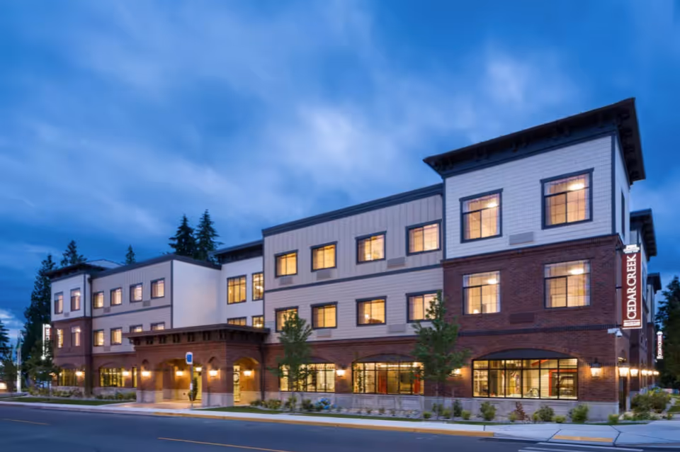Exterior view of Cedar Creek Memory Care Community building at dusk with lit windows.
