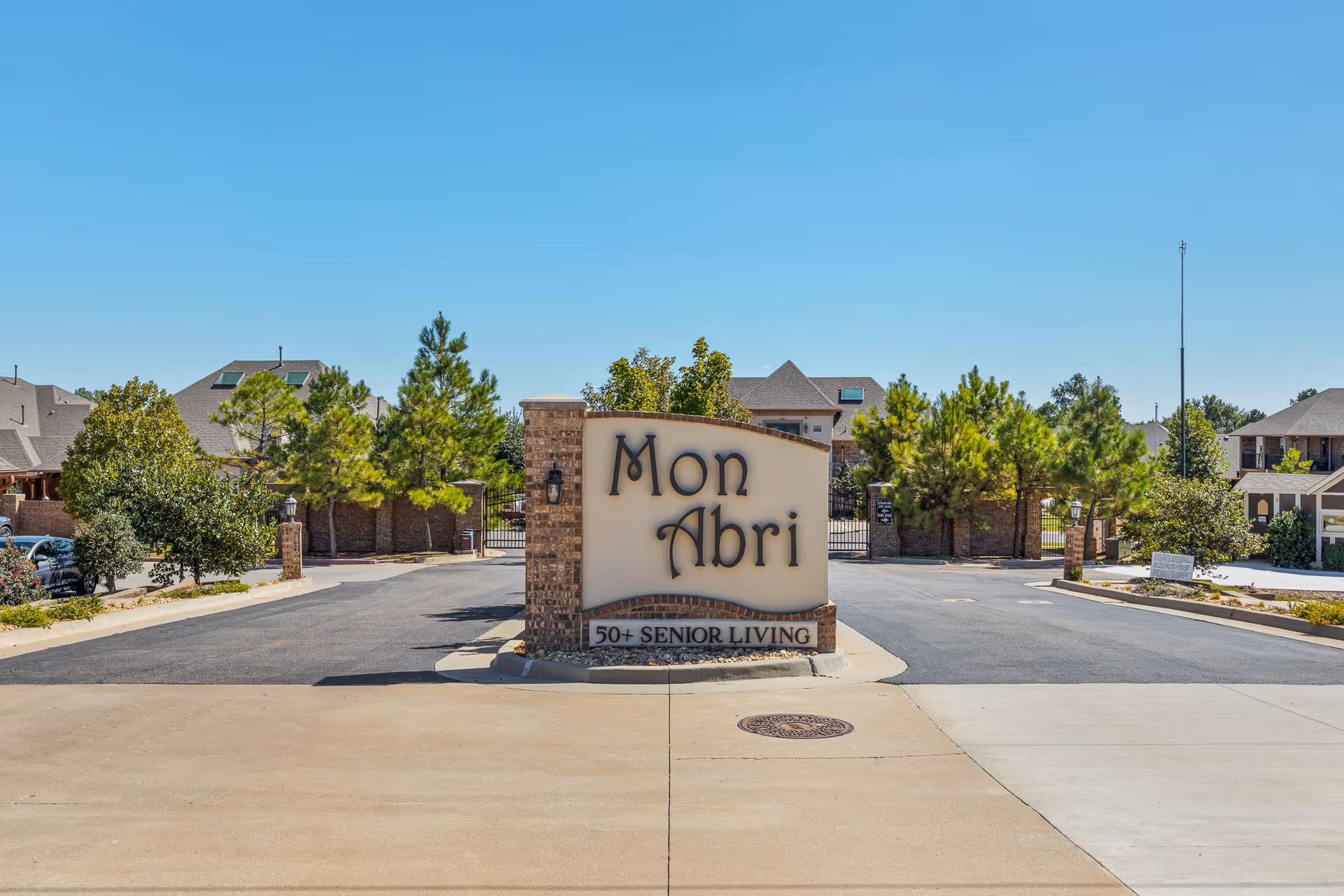 Entrance sign reading "Mon Abri 50+ Senior Living" at the gated driveway of a residential community.