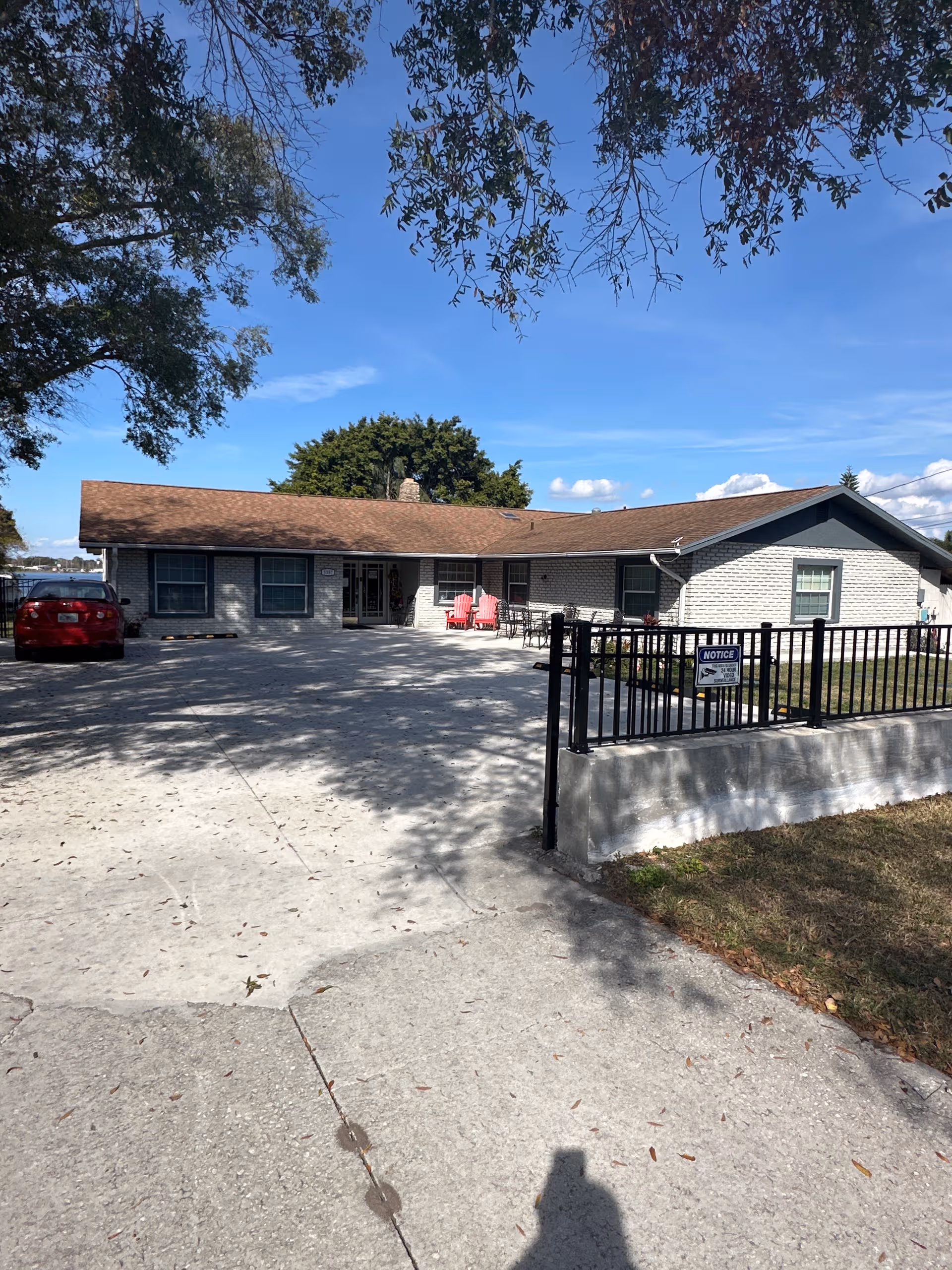 Lakeview Manor Assisted Living Facility front exterior with driveway, fence, and pink chairs.