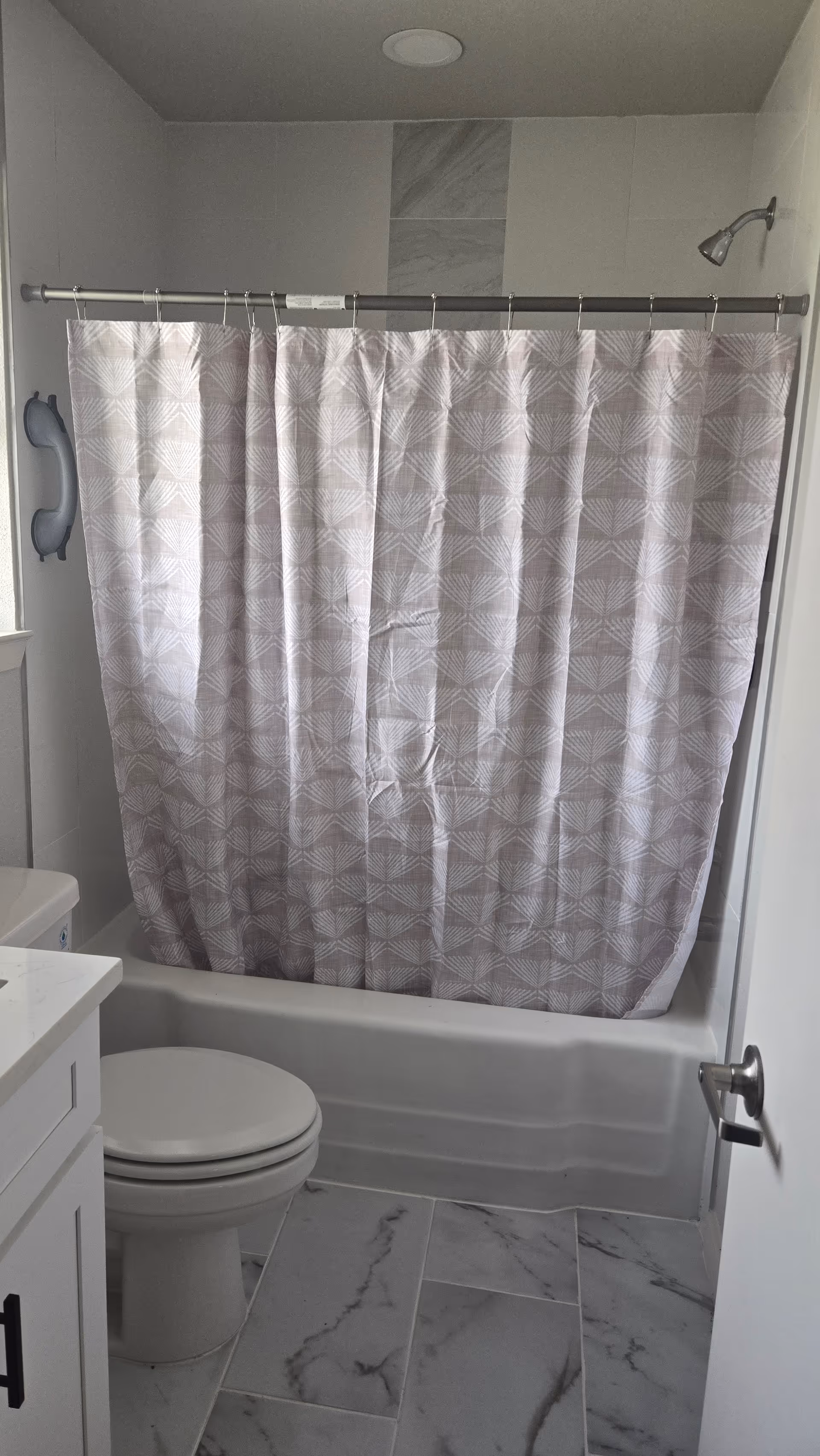 Small bathroom with a pink patterned shower curtain, toilet, sink, and marble floor.