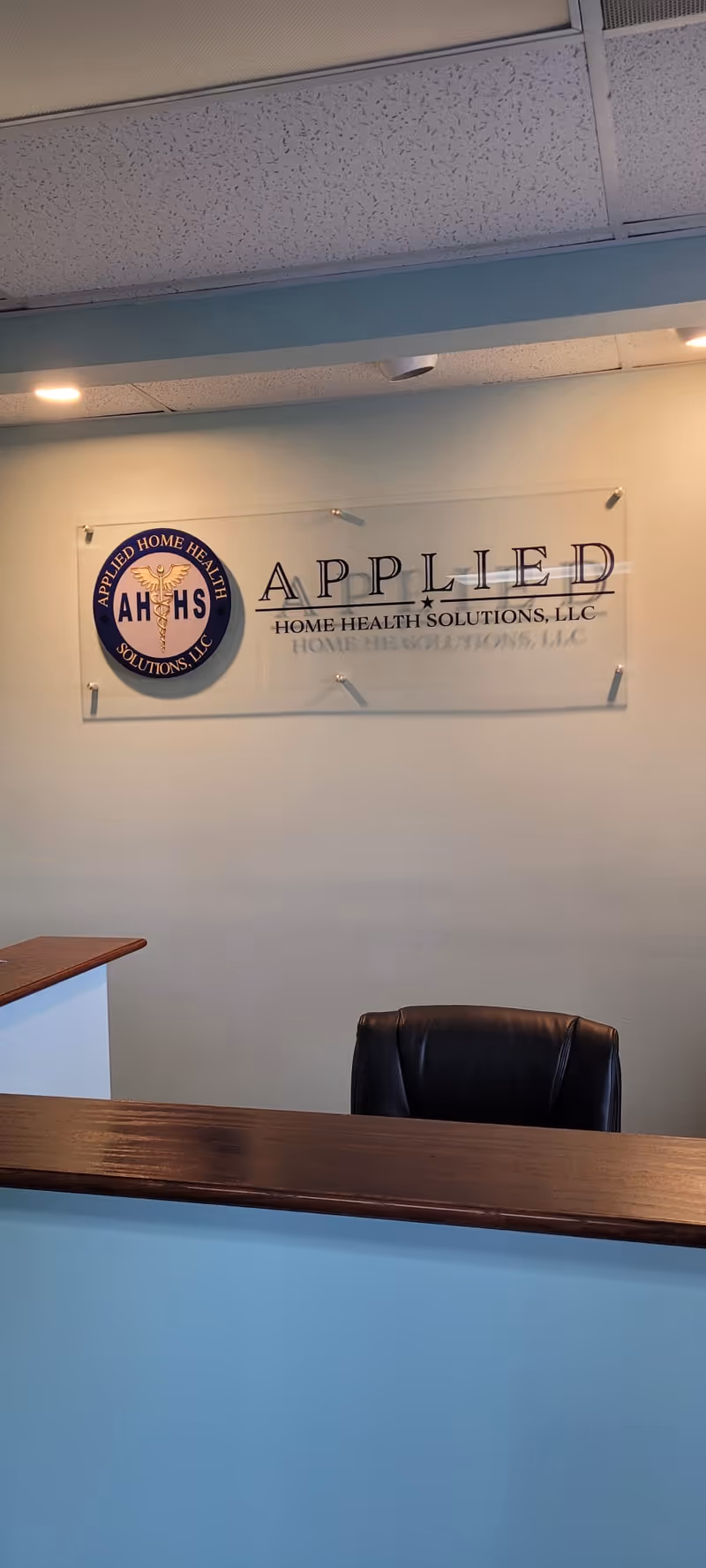 Reception desk with a black chair and wall sign reading Applied Home Health Solutions