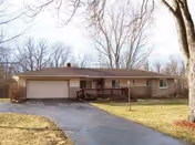 Single-story ranch-style house with an attached garage, front porch, driveway, and lawn with leafless trees.