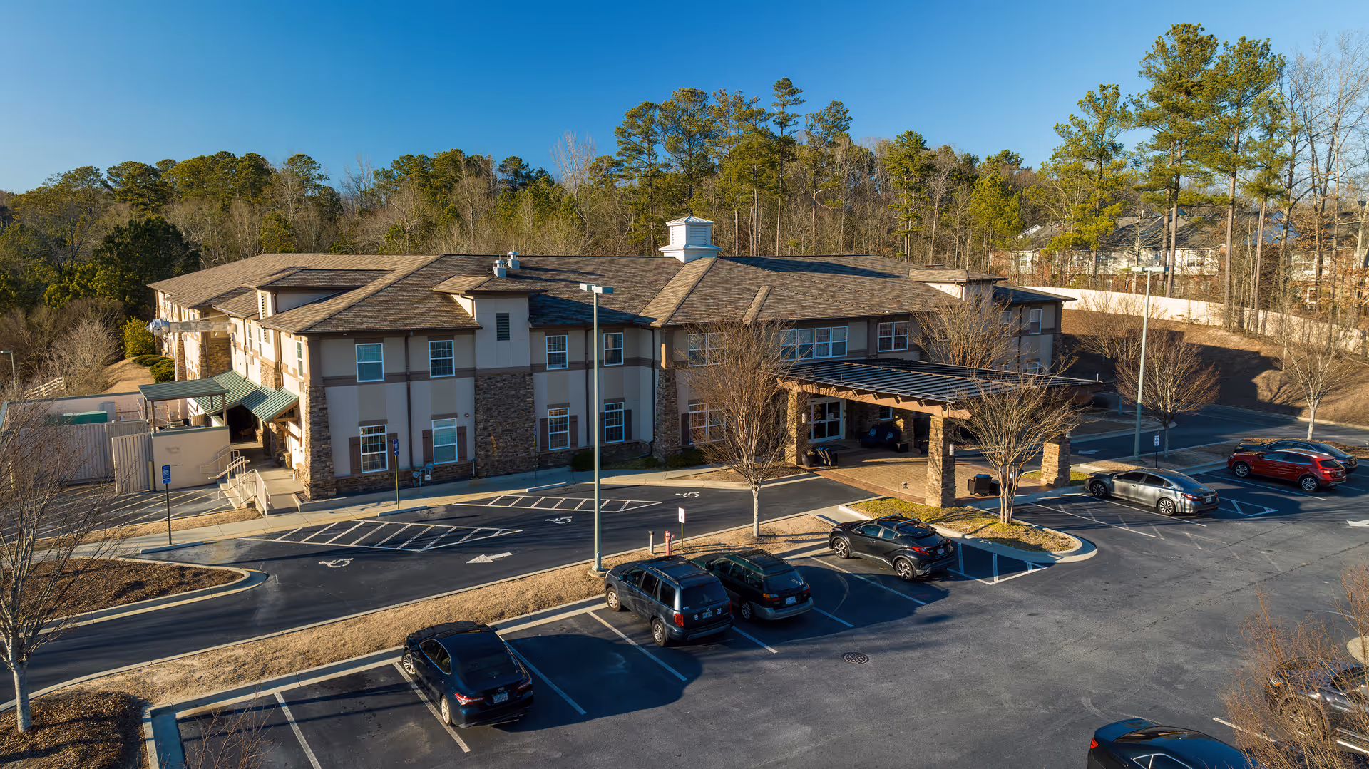 Aerial view of the Ivy Springs at Buford two-story senior living building with a covered entrance, parking lot, and surrounding trees.