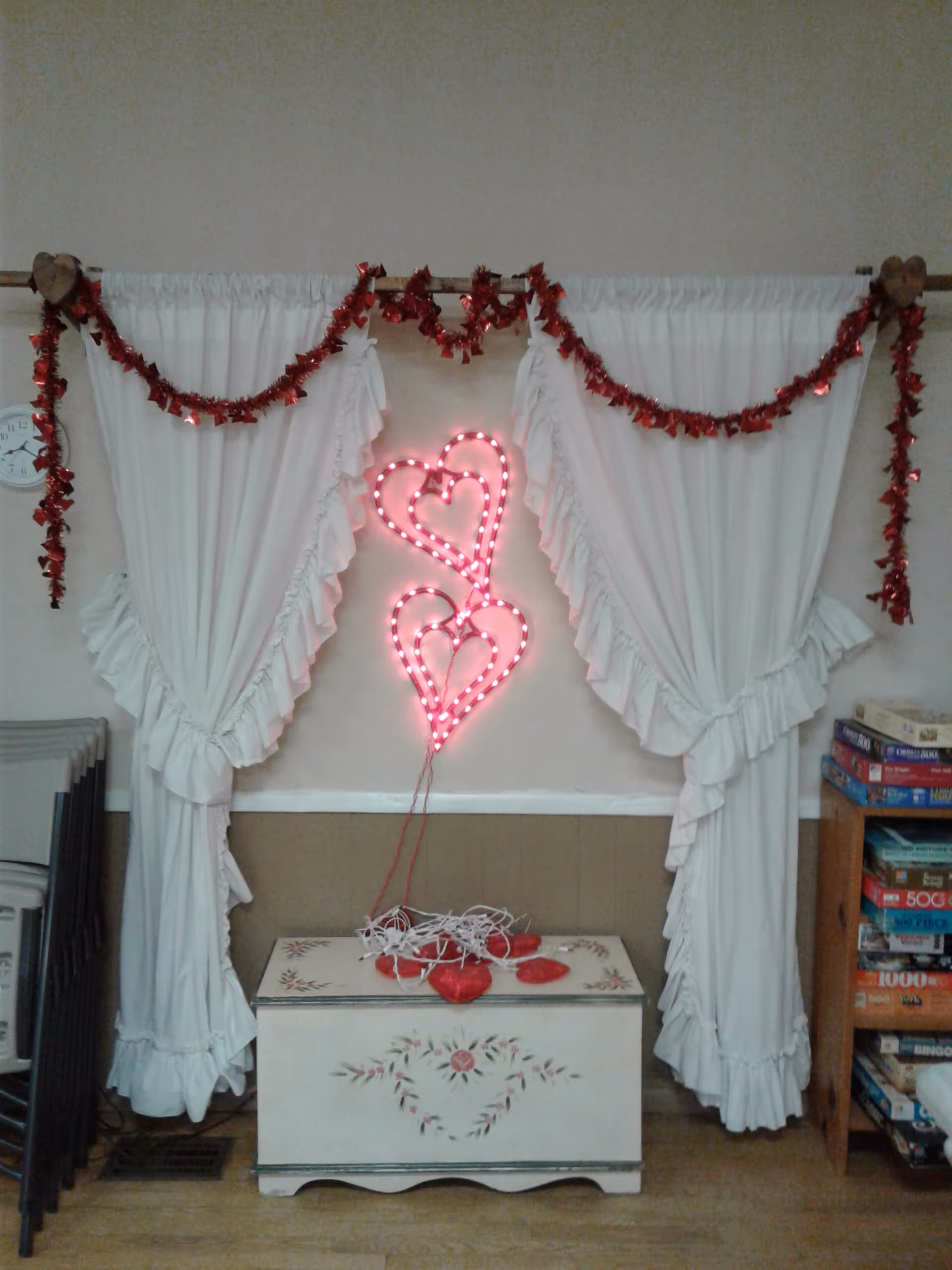 White draped centerpiece with red garlands and pink heart neon lights over a floral chest.