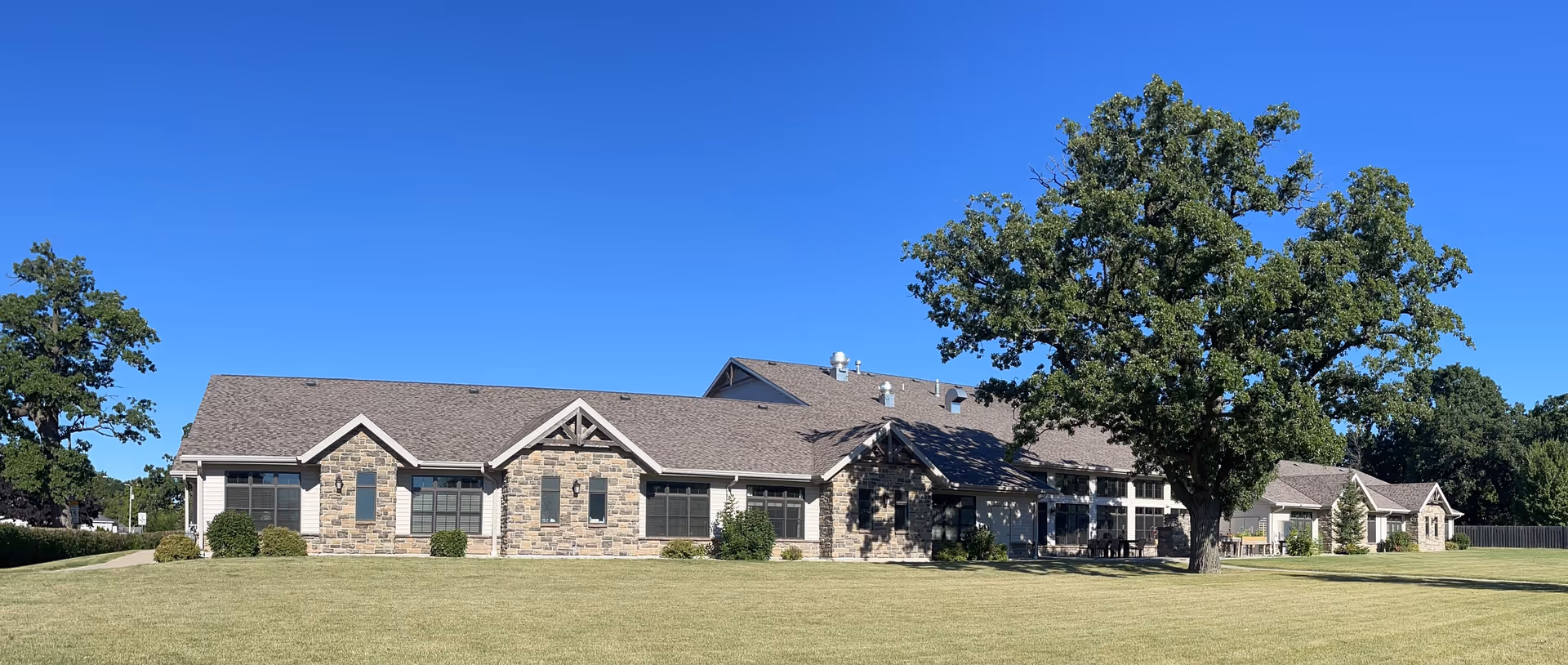 A single-story stone-faced senior living facility with a manicured lawn and trees.