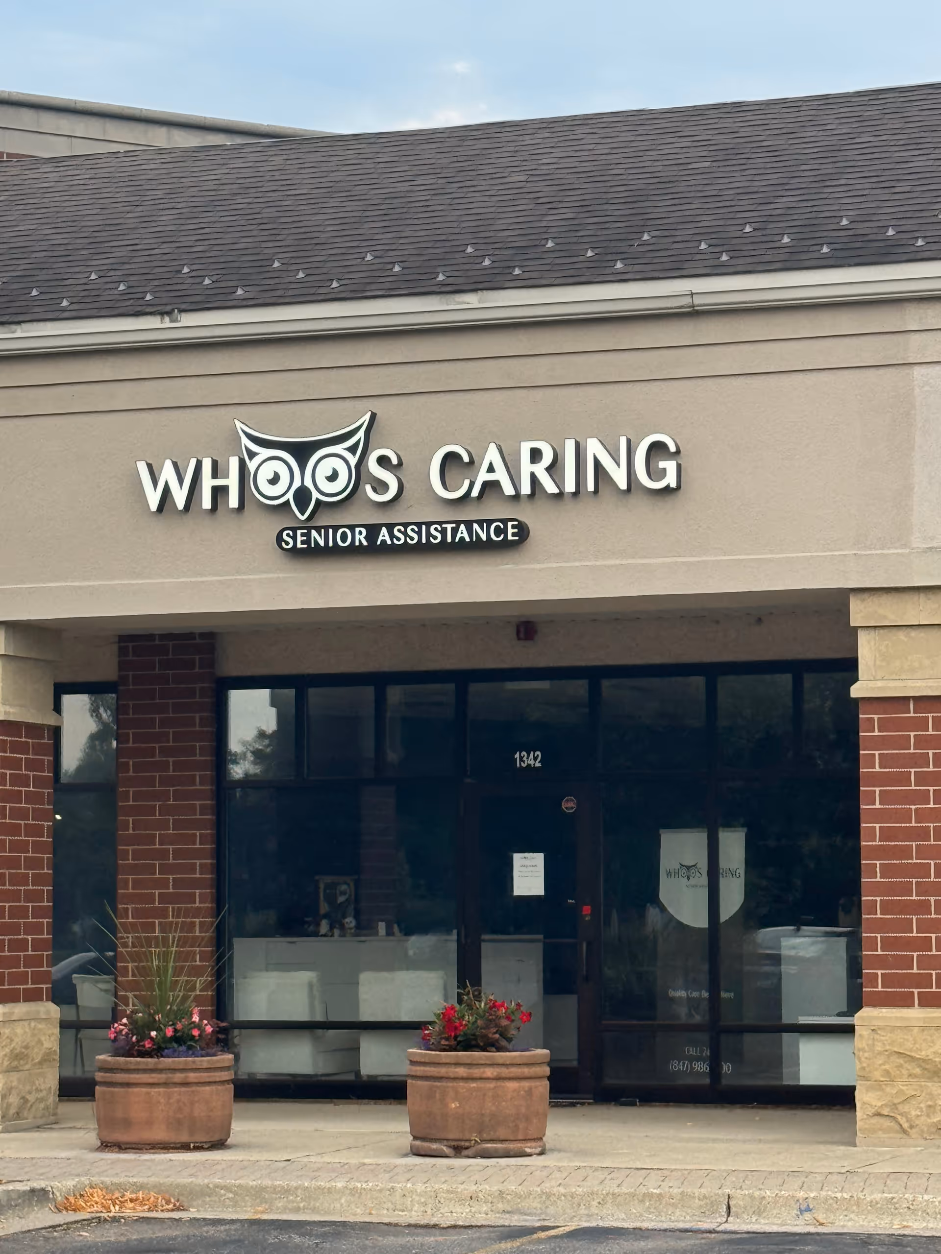 Exterior view of a senior care facility storefront with sign Whoo's Caring and potted plants.
