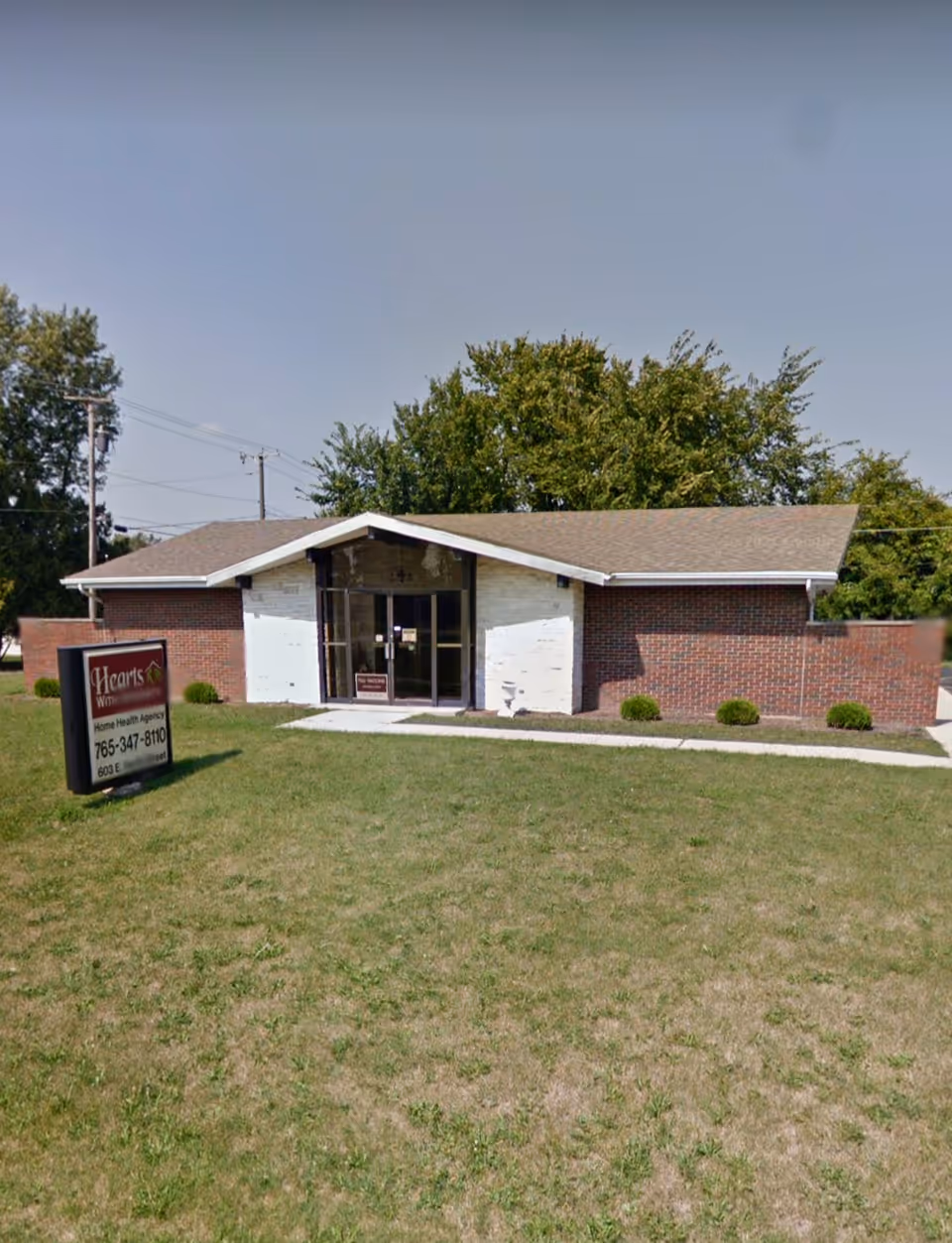 A single-story brick building with glass doors, a sign, and a grassy front lawn.