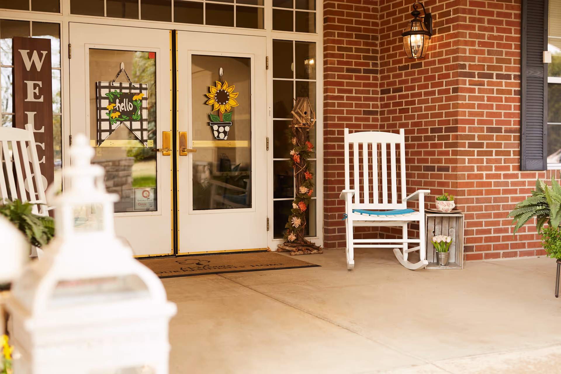 Entrance of Trustwell Living of Springfield with brick exterior, glass doors, chair, and plants.