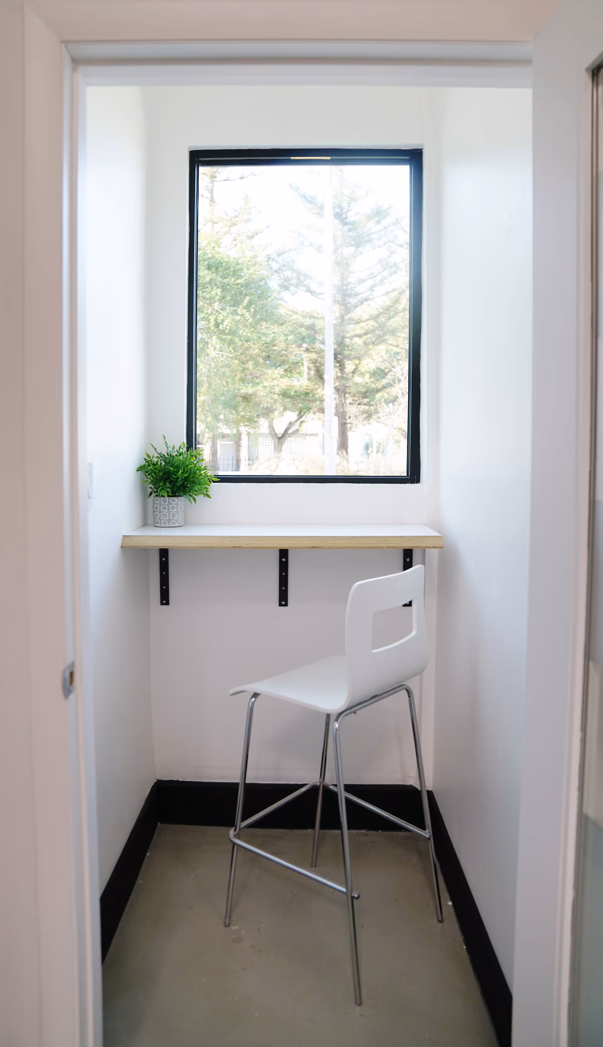 Small white interior nook with window, wall-mounted shelf, plant, and white chair.